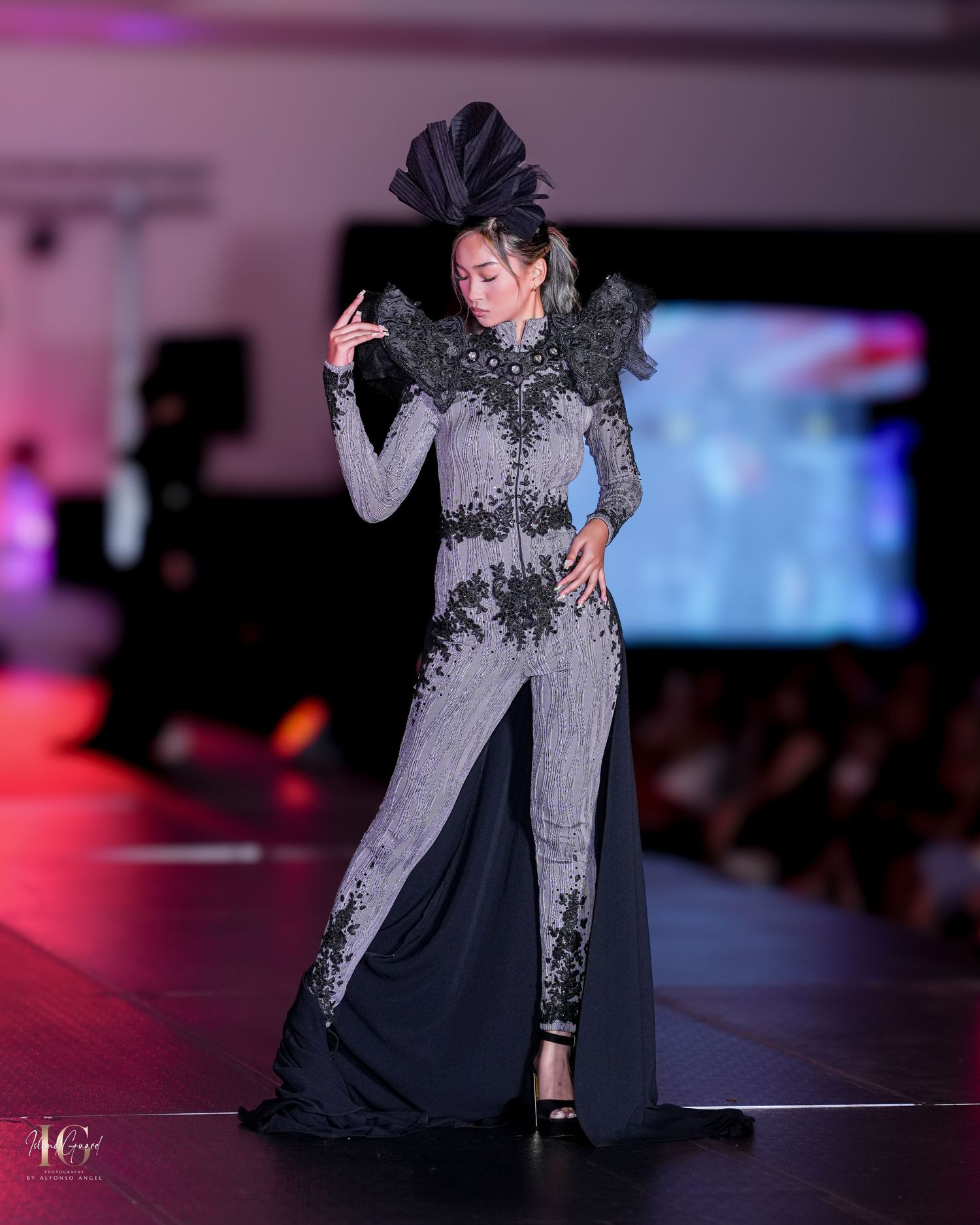 Model in grey and black evening gown with dramatic black feathered headpiece on catwalk.