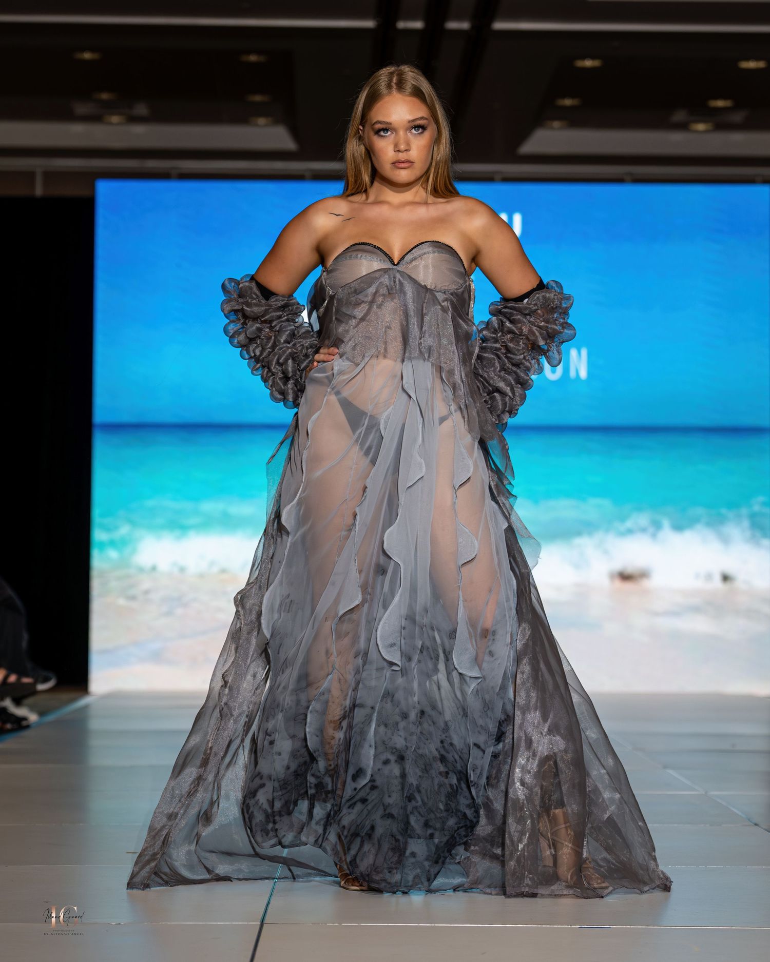Dramatic gray tulle gown with sweetheart neckline and ruffled details shown at beachside fashion show.