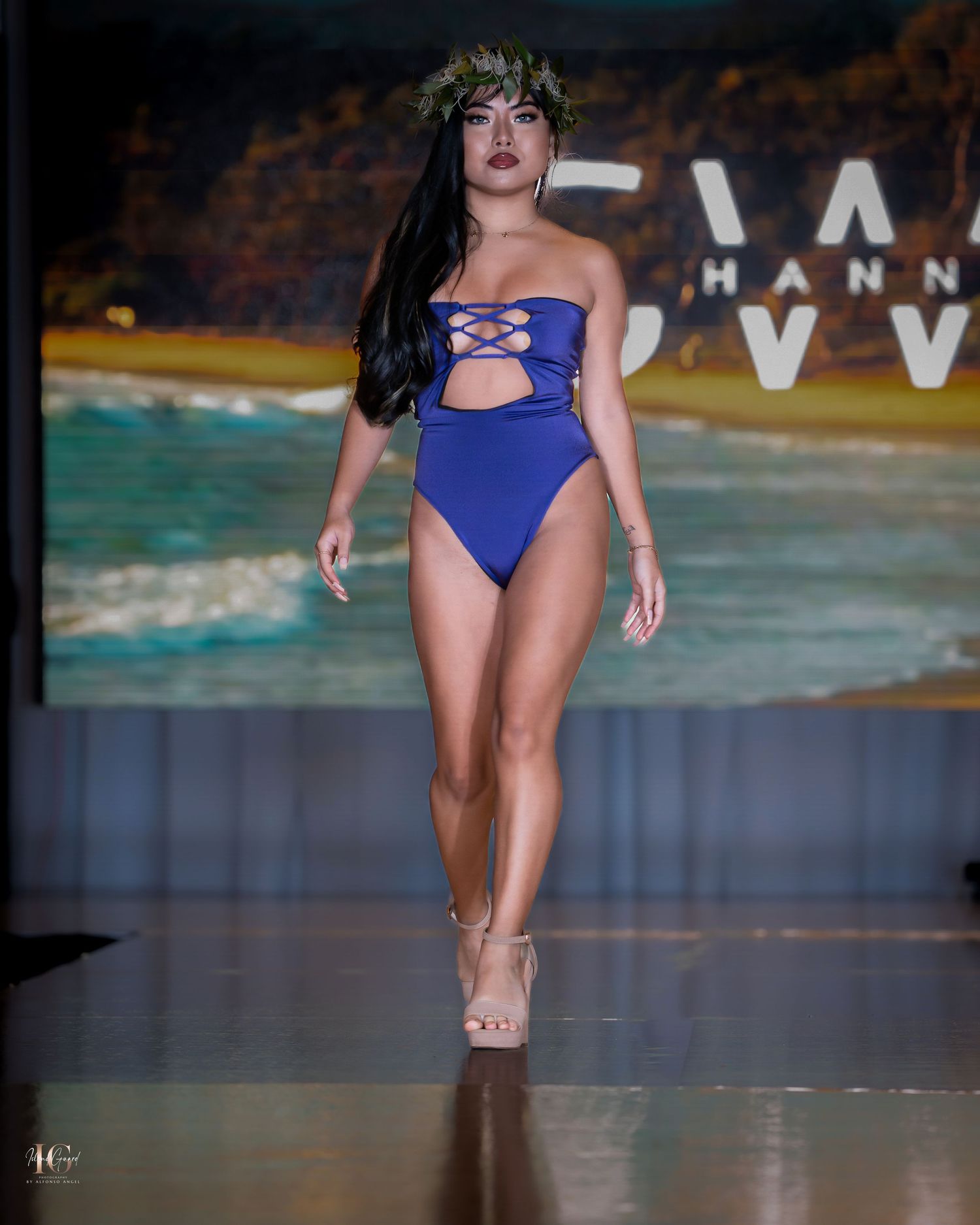 Royal blue cutout swimsuit presented on beach-themed runway backdrop.