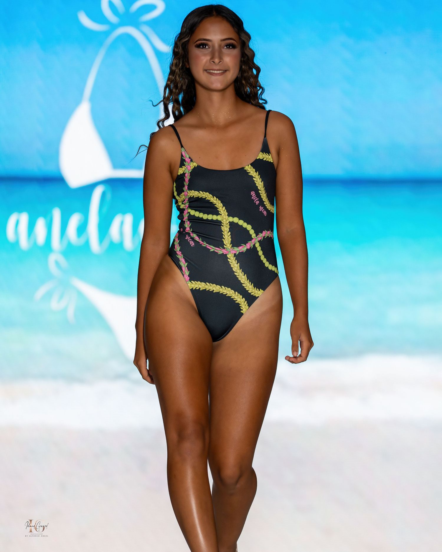 Model walks runway in black one-piece swimsuit with yellow chain pattern design.