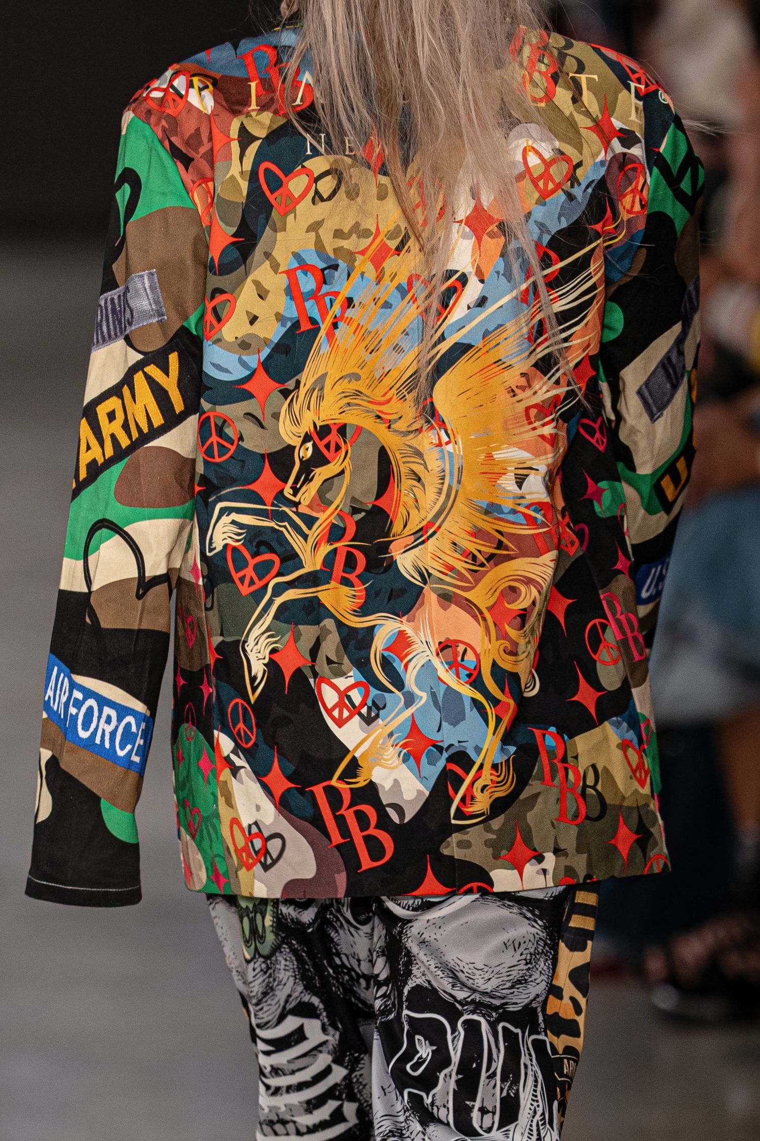 Colorful abstract patterned fashion garments displayed on models walking down a runway during a fashion show.