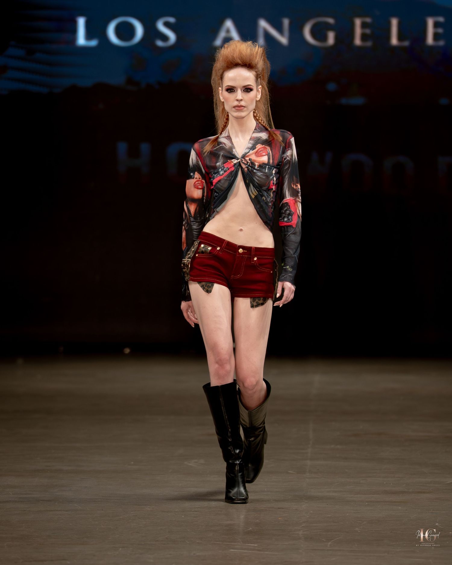 Model walks runway in black leather boots and red floral outfit during Los Angeles Fashion Week show.