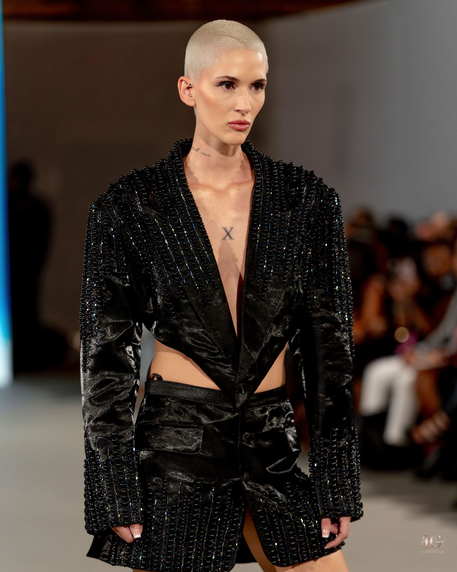 Model walks runway in sparkling black blazer dress with structured shoulders at fashion show.