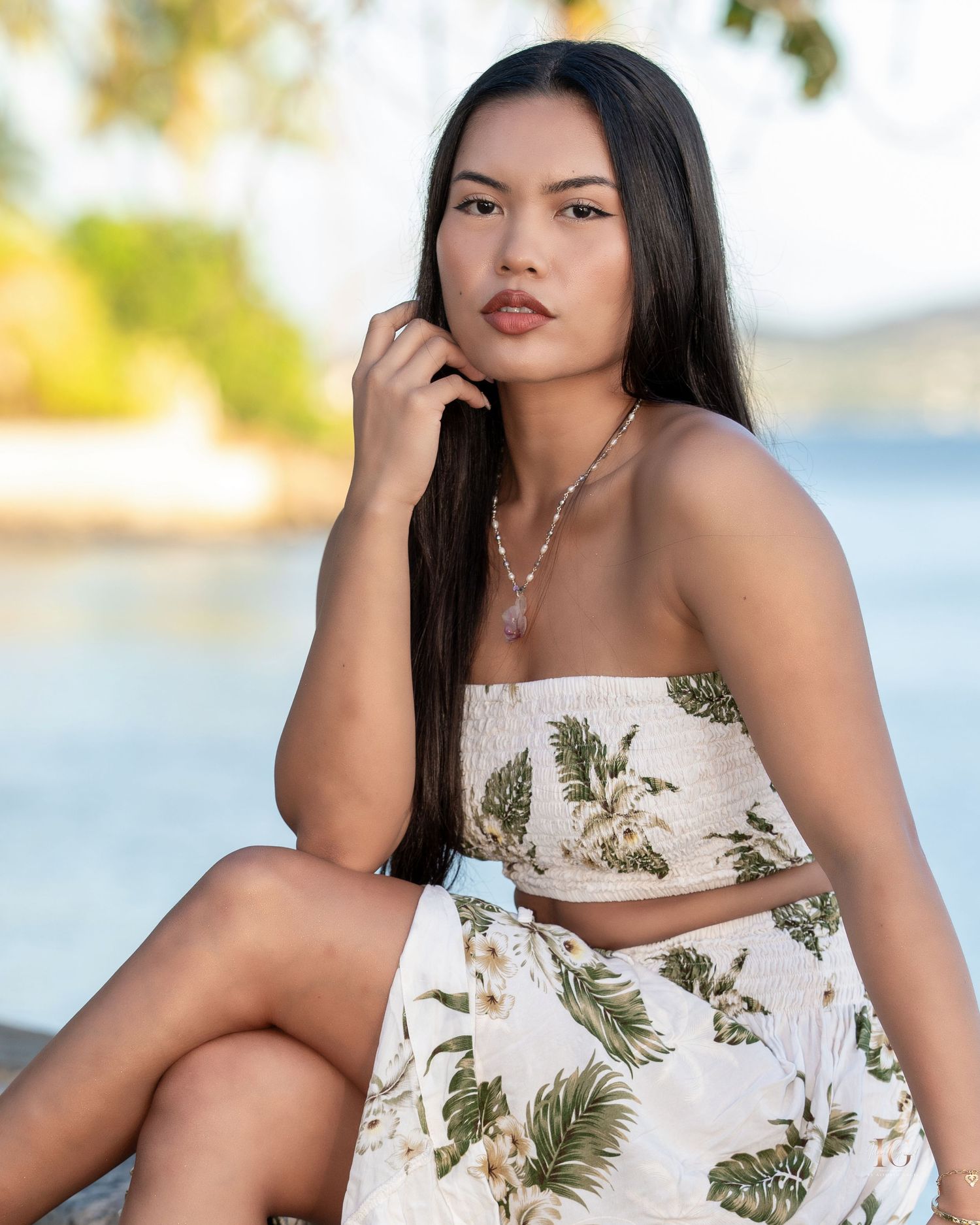 A woman in a tropical print two-piece outfit poses outdoors by the water on a sunny day.
