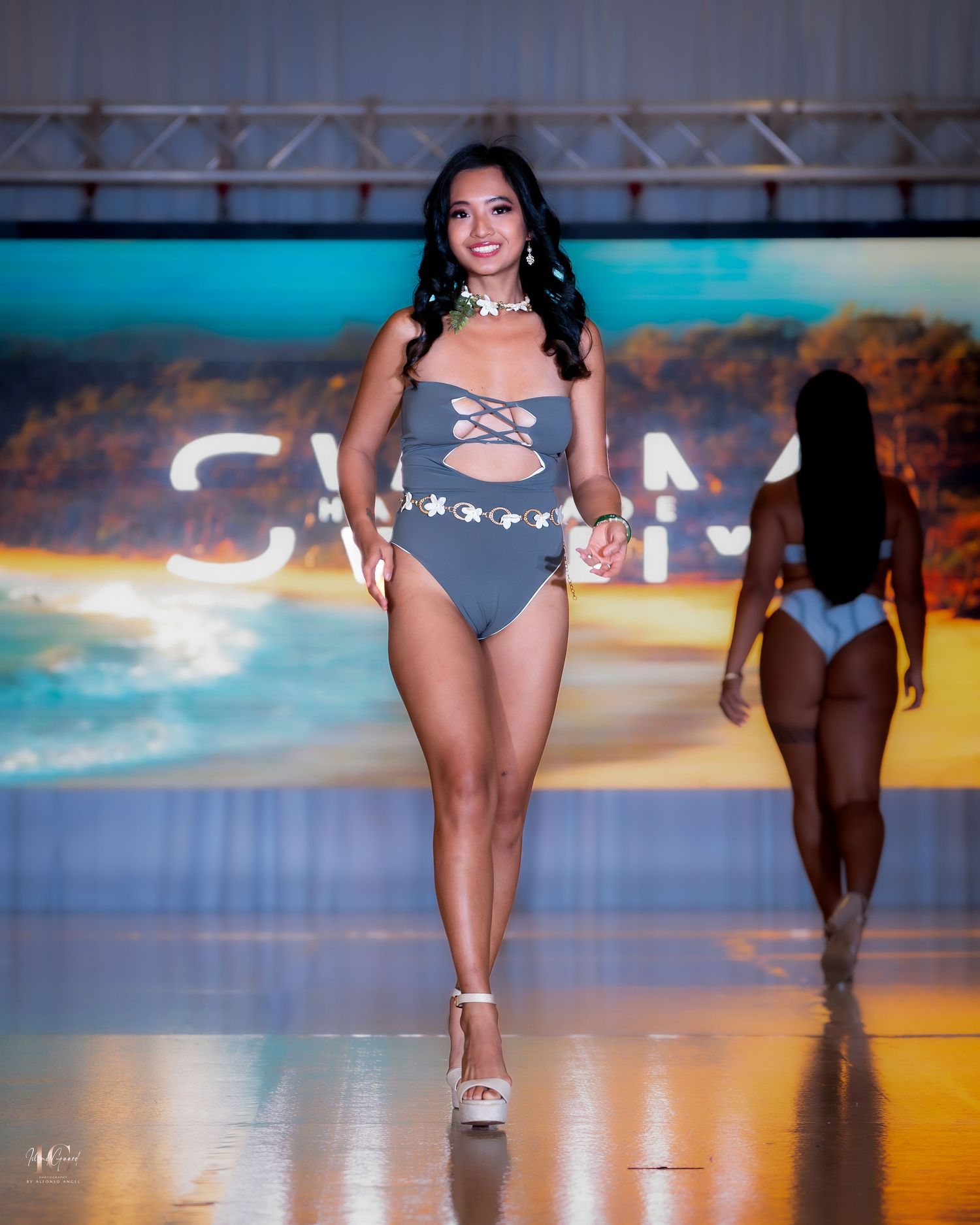 Models walk the runway in gray swimwear during a fashion show with dramatic sunset lighting.