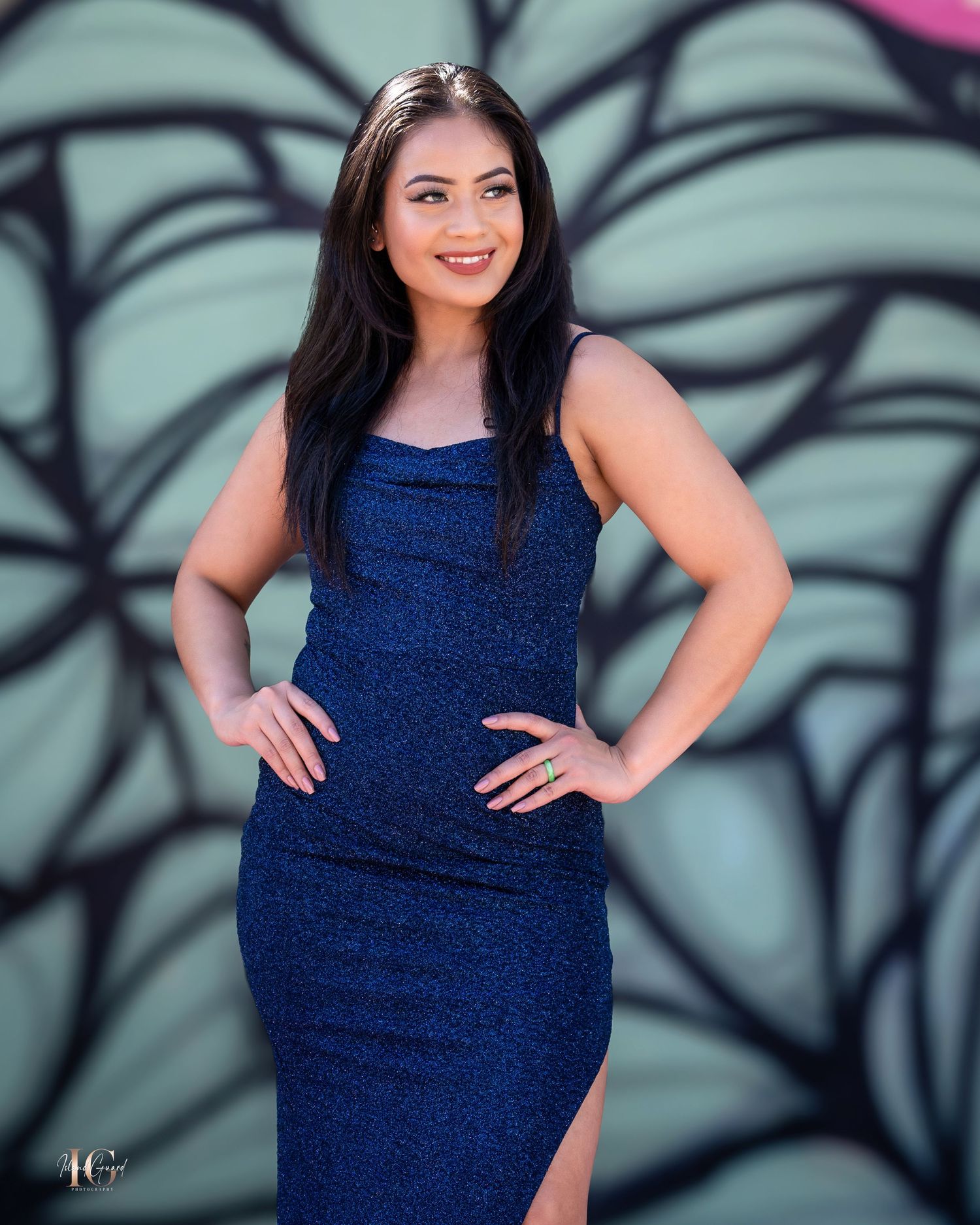 Model wearing navy blue dress poses against artistic swirl patterned wall.