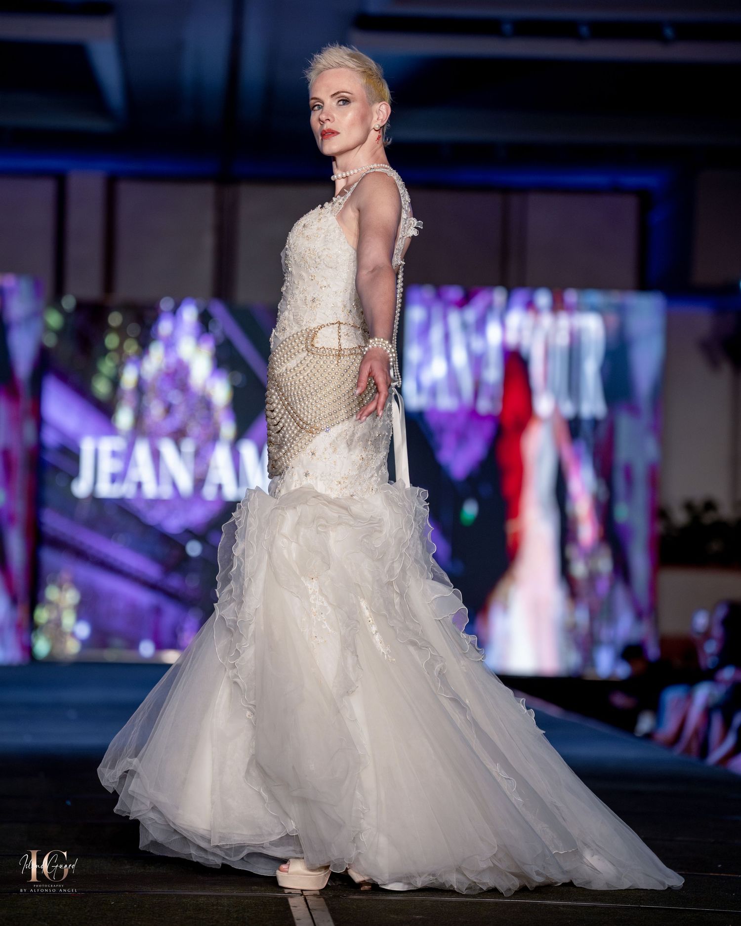 Mermaid-style wedding dress with fitted bodice and ruffled tulle train displayed at evening fashion show.