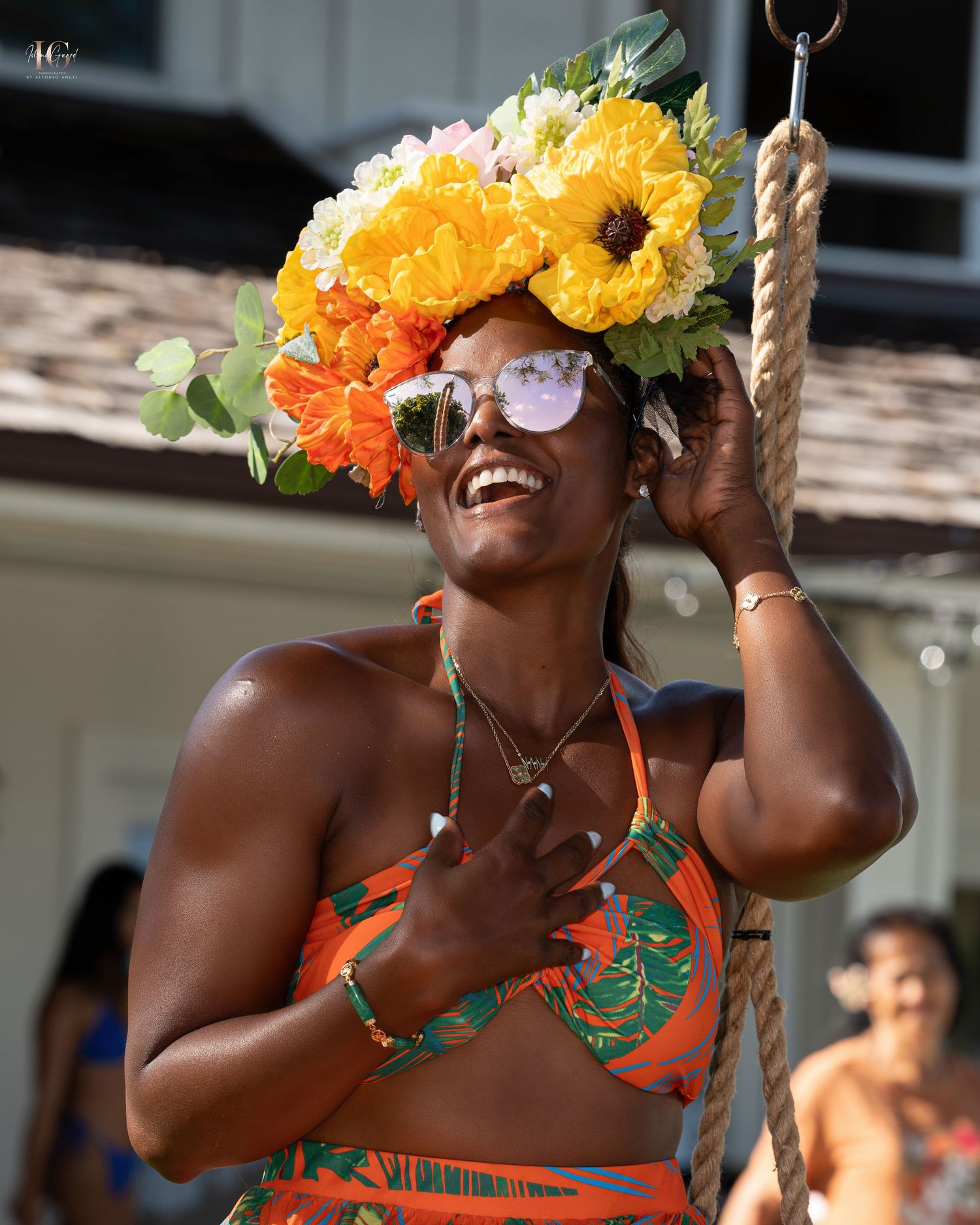 A person wearing vibrant yellow and orange floral crown laughs joyfully while holding onto a rope swing outdoors.