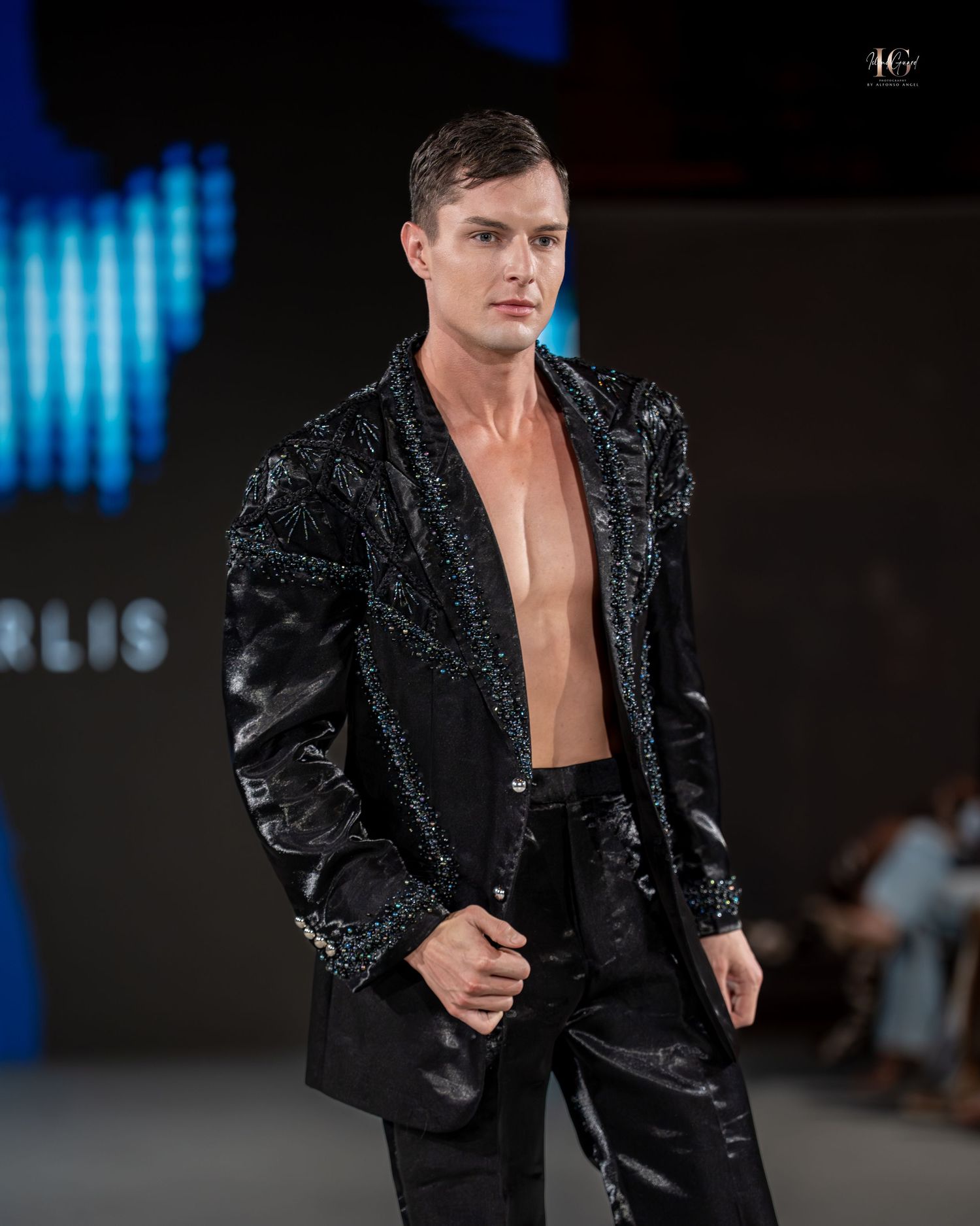 A model walks the runway wearing a black sequined blazer and black pants at a fashion show.