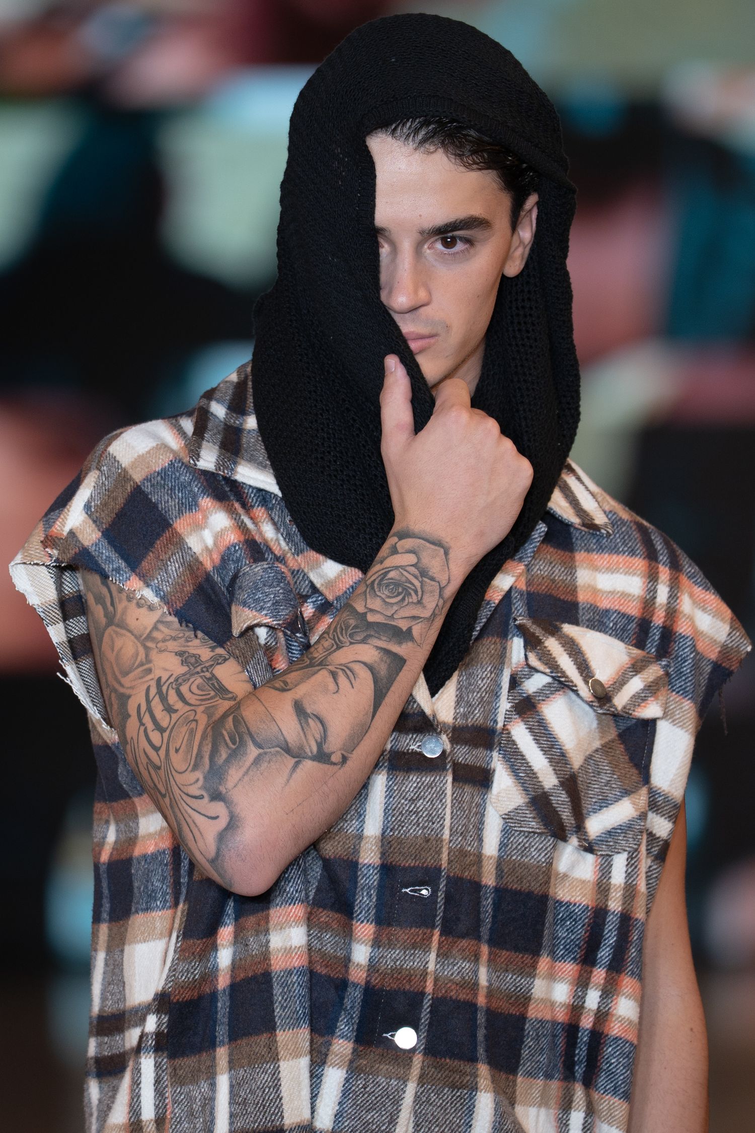 Series of close-up shots showing a person in a plaid flannel shirt and black hood with visible arm tattoos.