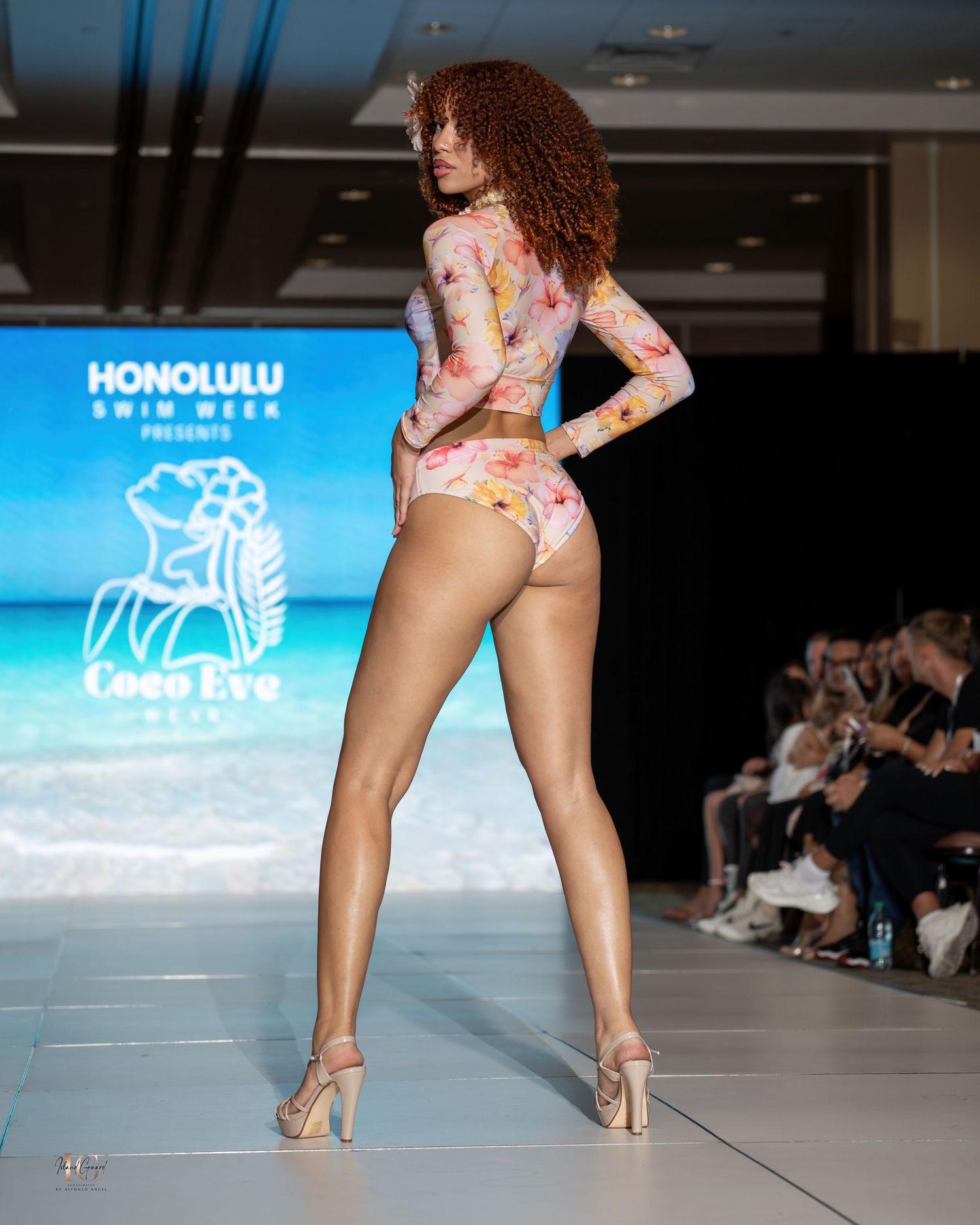 Back view of model in floral print swimwear walking runway at fashion show.