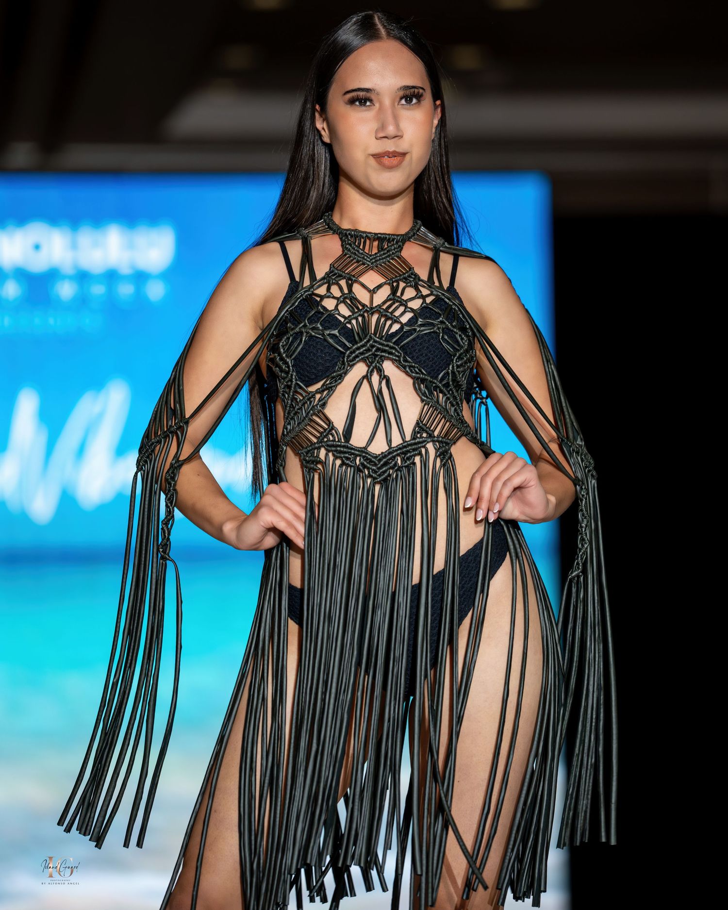 Black fringe swimsuit design showcased on beachwear runway with tropical backdrop.