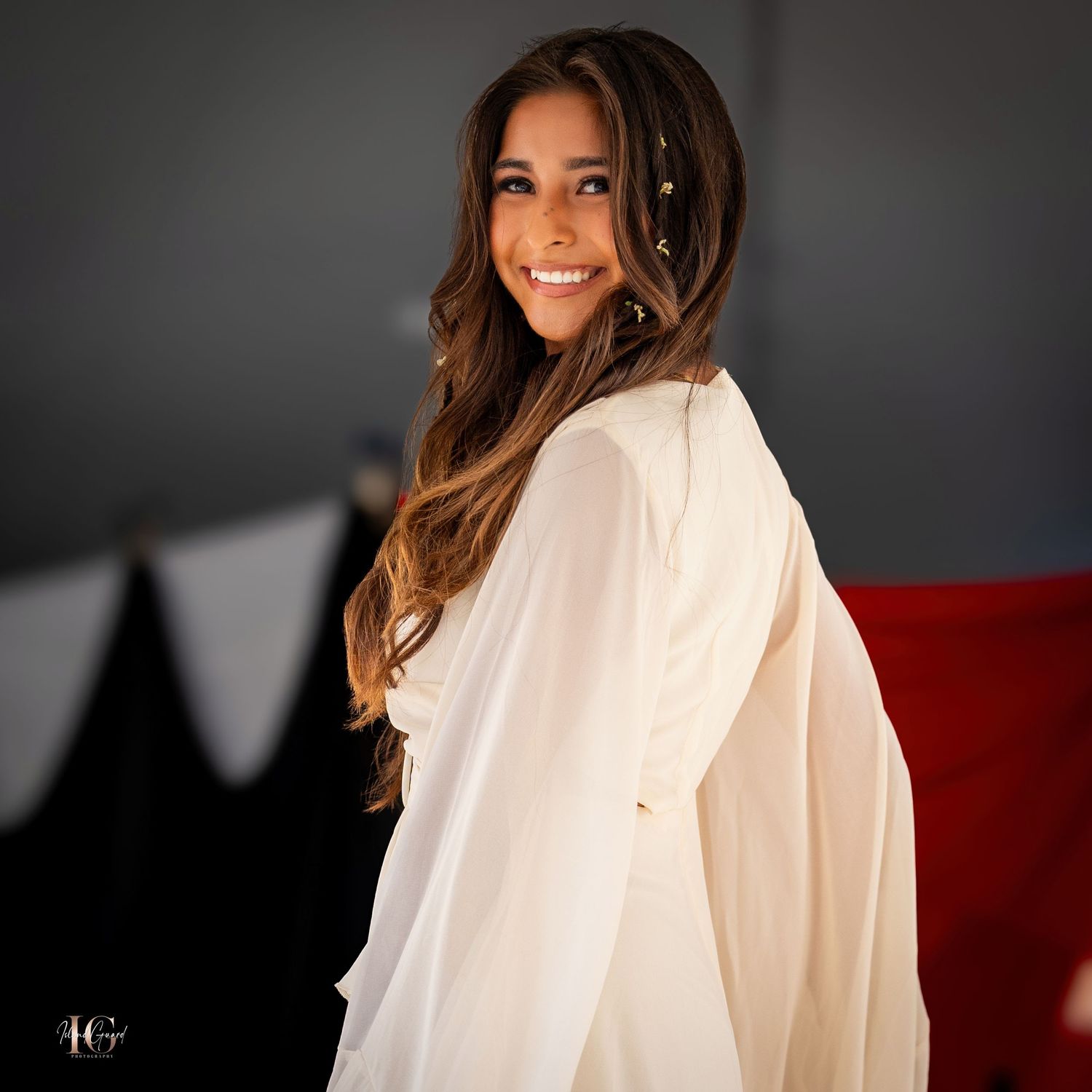 Portrait of model in cream colored flowing top with styled waves against dark background.