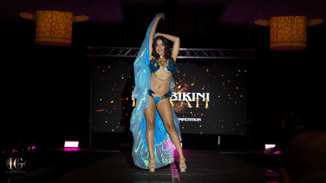 Fashion models showcase vibrant swimwear designs on a dark runway stage with dramatic lighting and decorative elements.