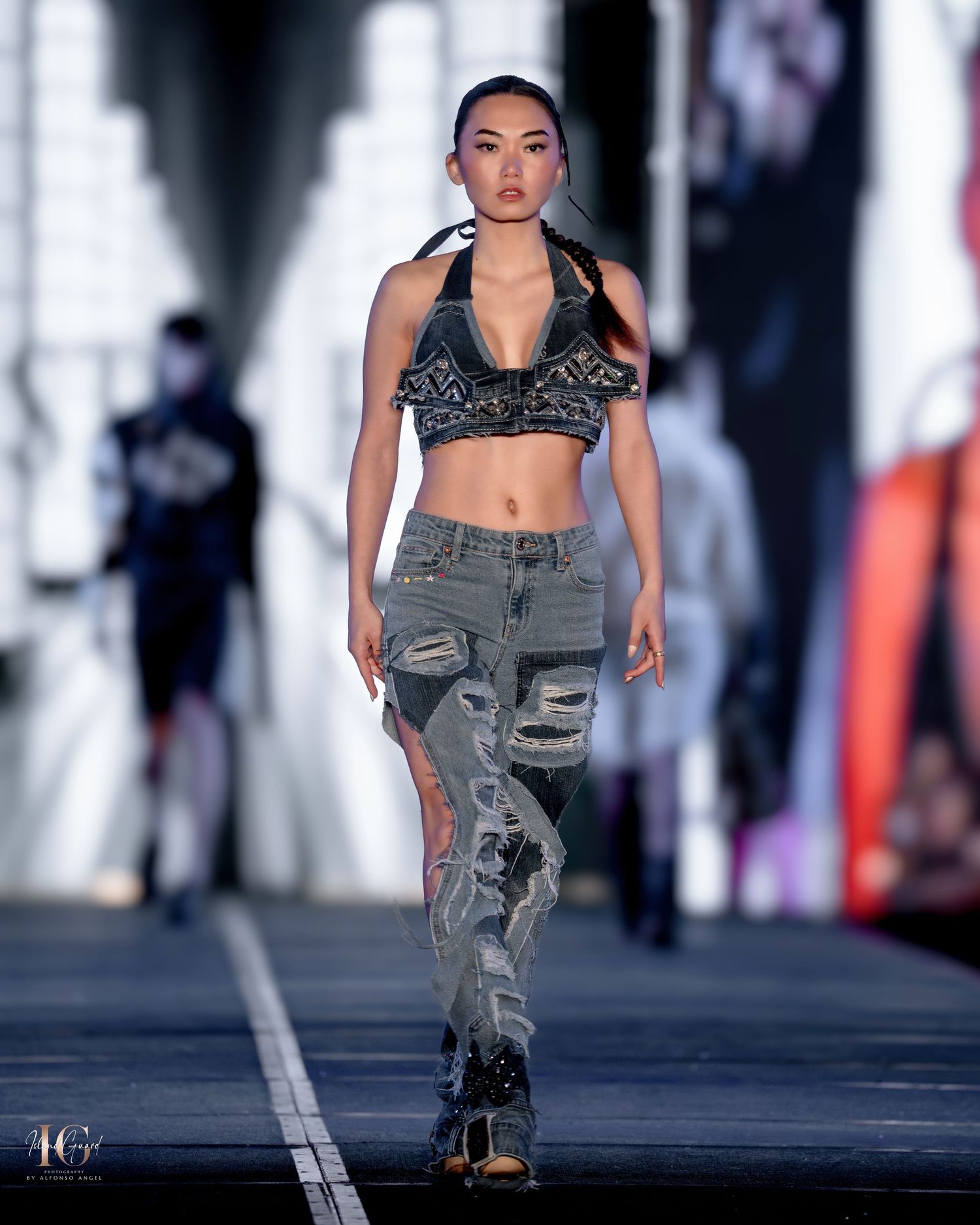 Model presents distressed denim and sparkly crop top combination on fashion runway.