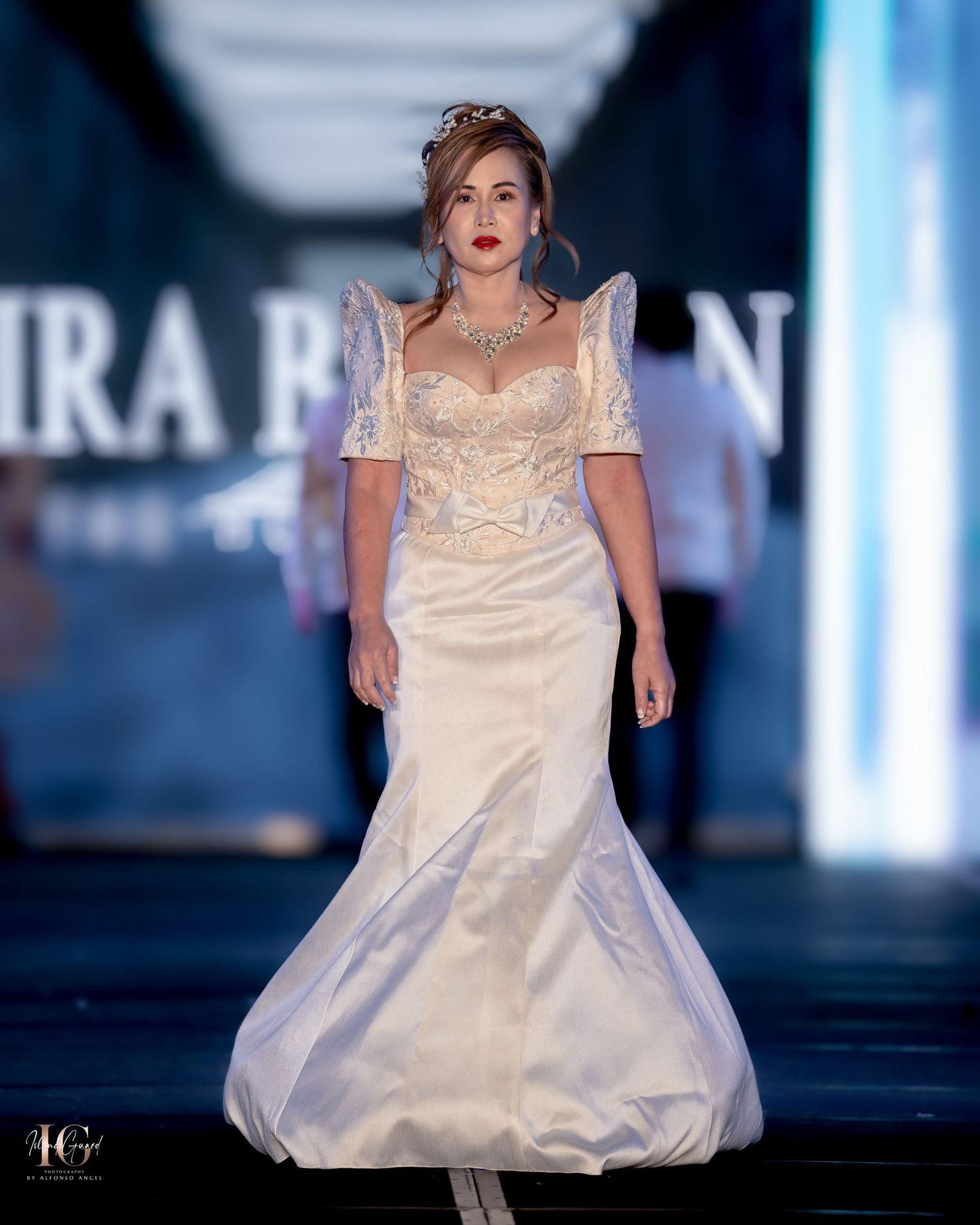 Model showcases voluminous white formal gown on illuminated fashion runway.