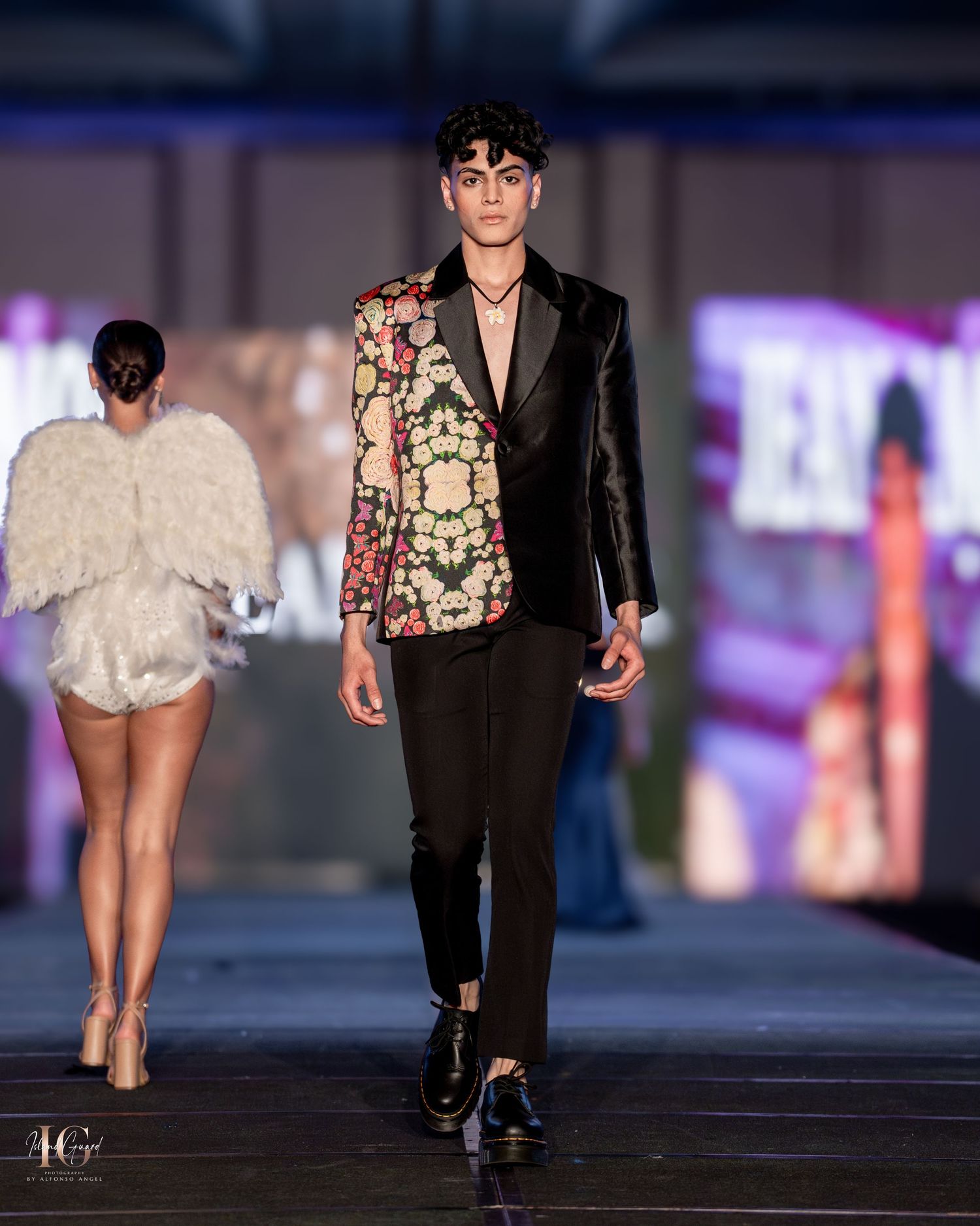 Fashion show models showcase contrasting black and white outfits on dimly lit catwalk.