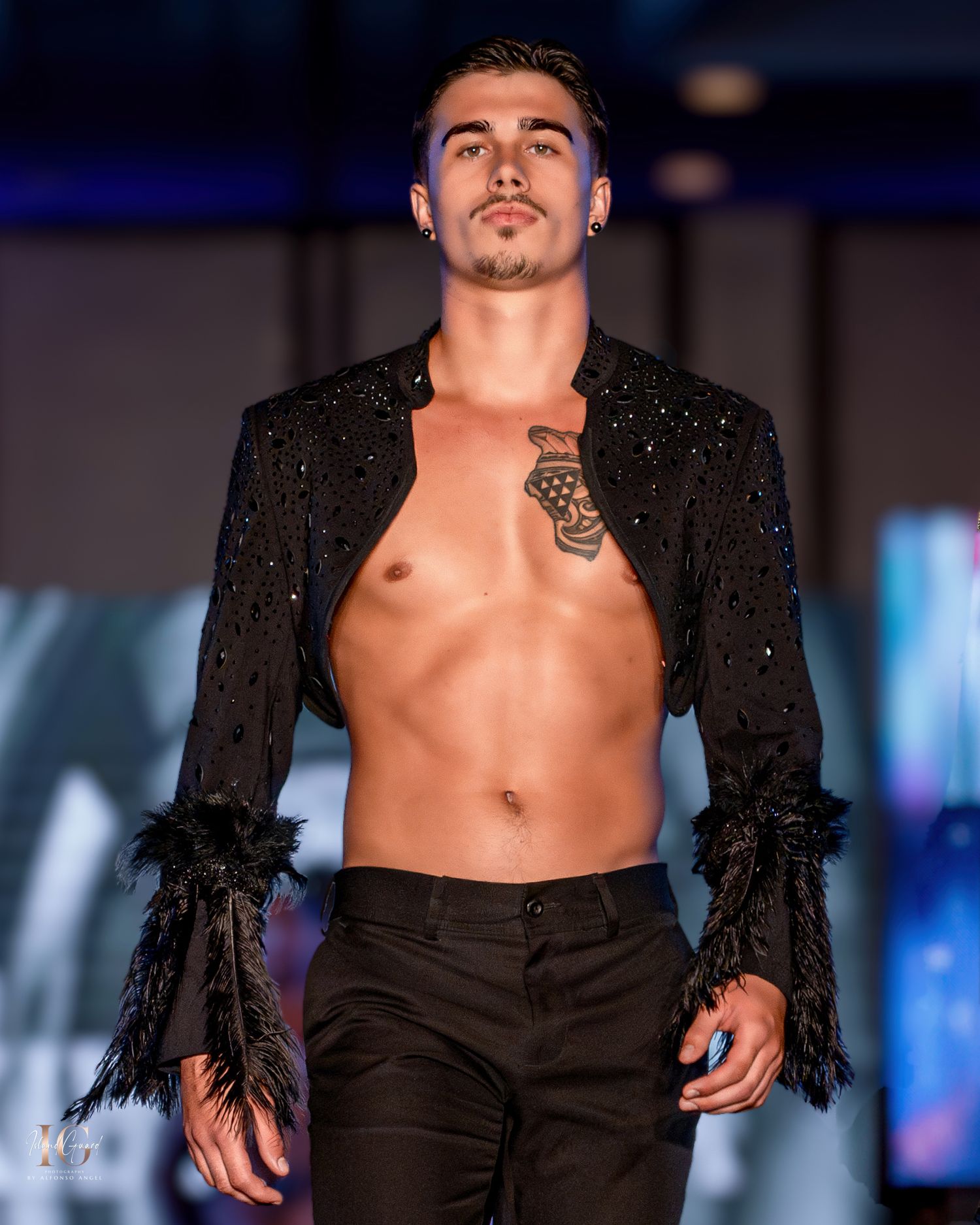 Model showcases shimmering black open jacket with feathered cuffs on fashion runway.