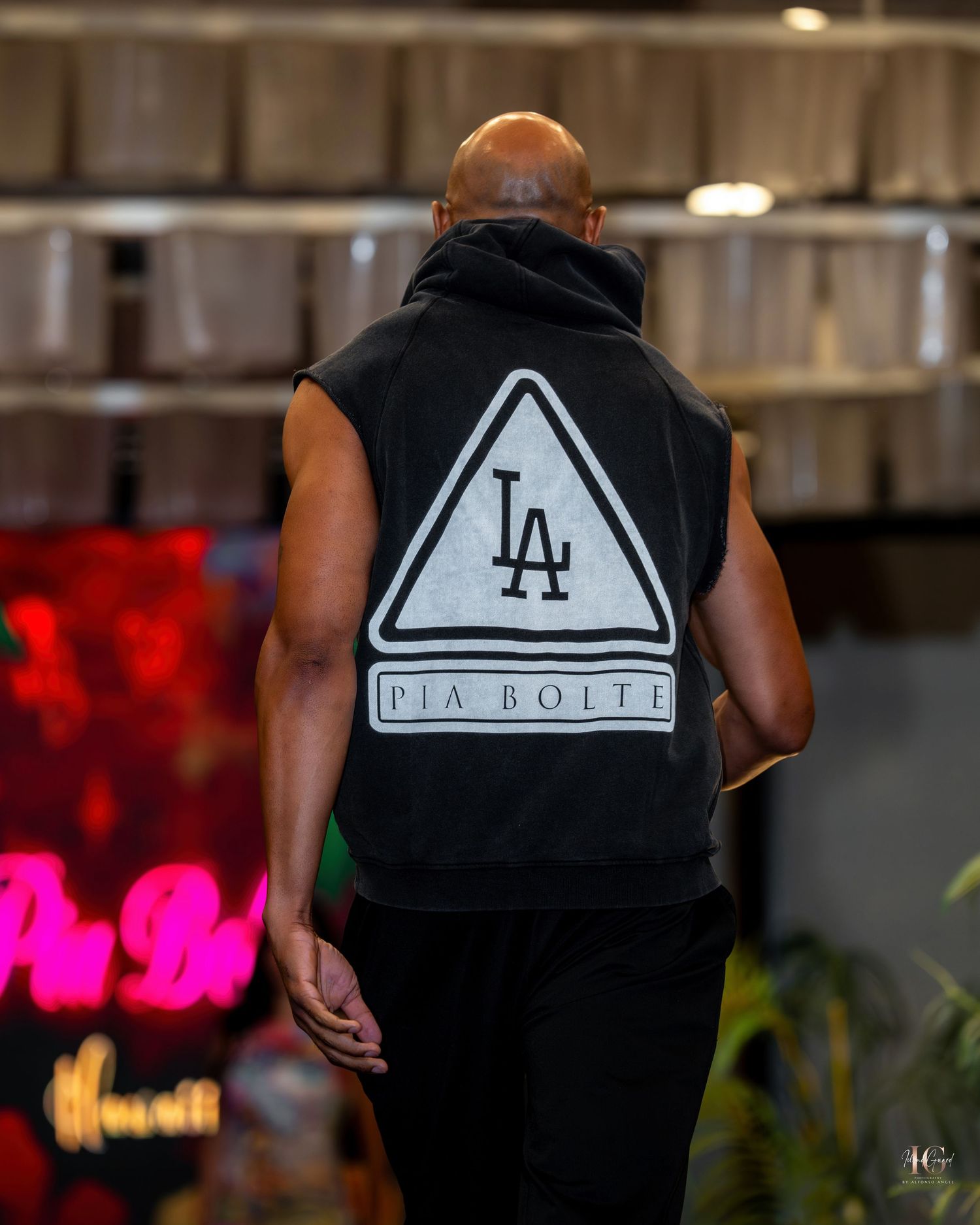 Person wearing black vest with white triangle logo design walking through indoor space with colorful lighting.