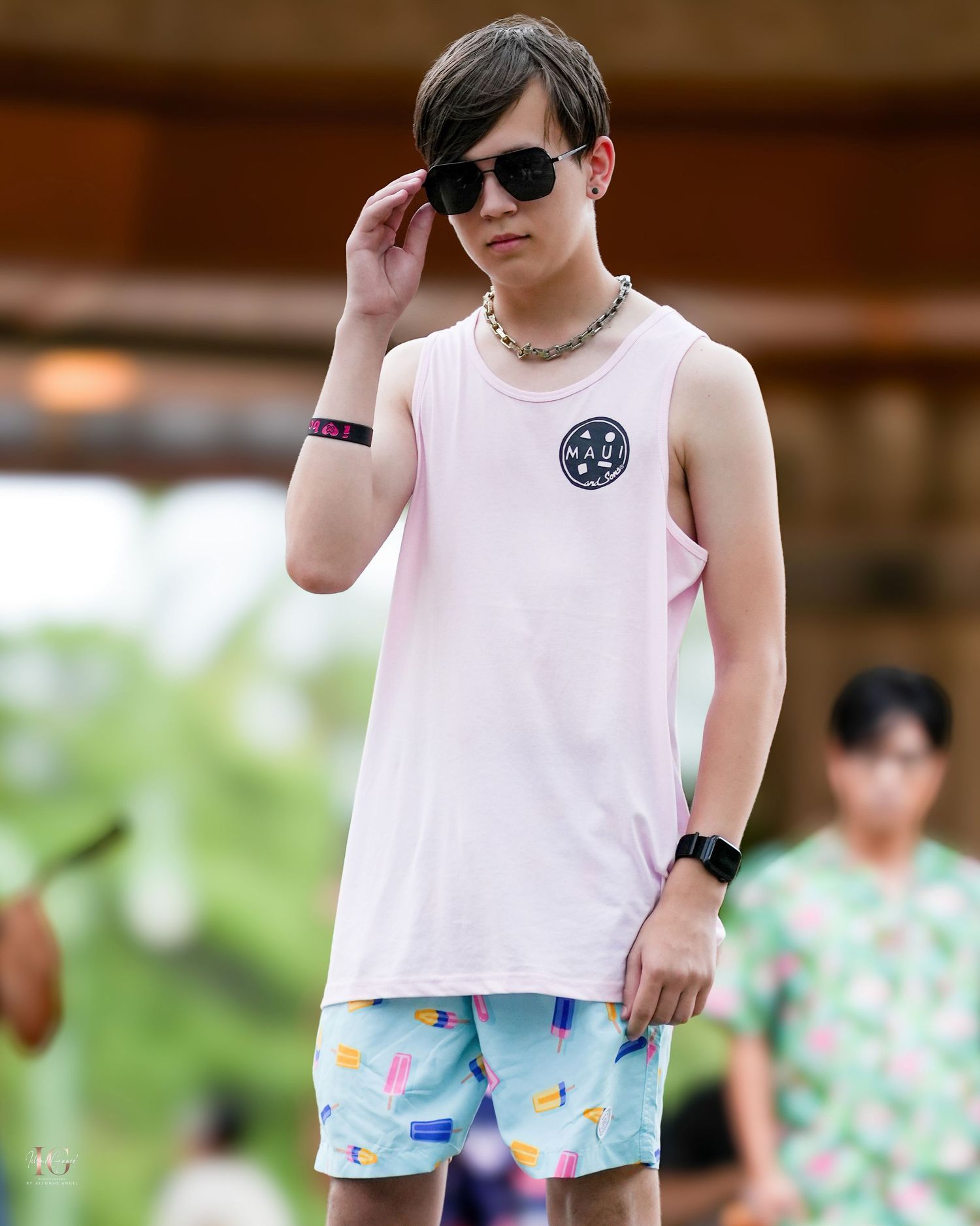 A person in a white tank top and floral print shorts stands outdoors in a casual summer outfit.