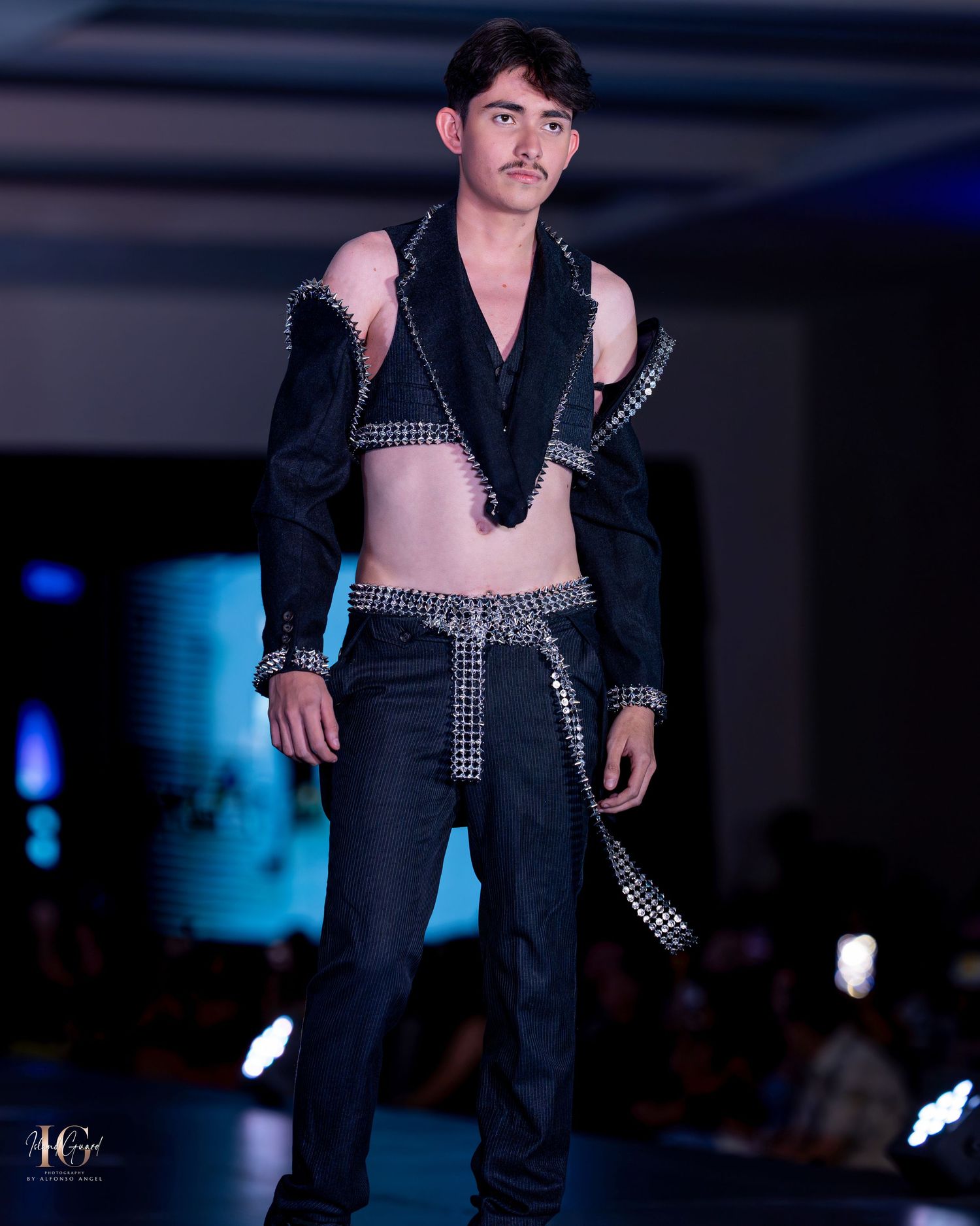 Fashion model struts in black modern streetwear ensemble with metallic accents on catwalk.