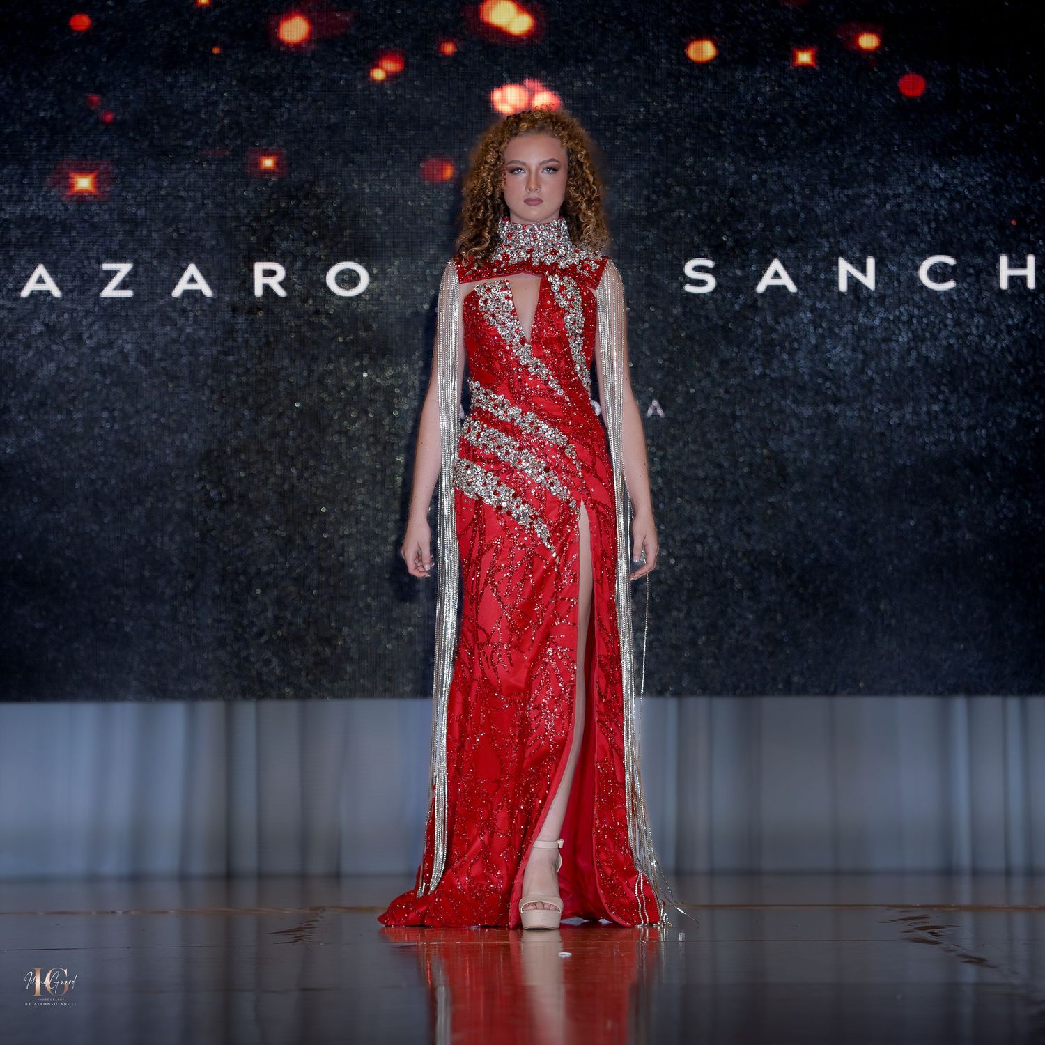 Red sequined evening gown with diagonal silver embellishments displayed at fashion show.