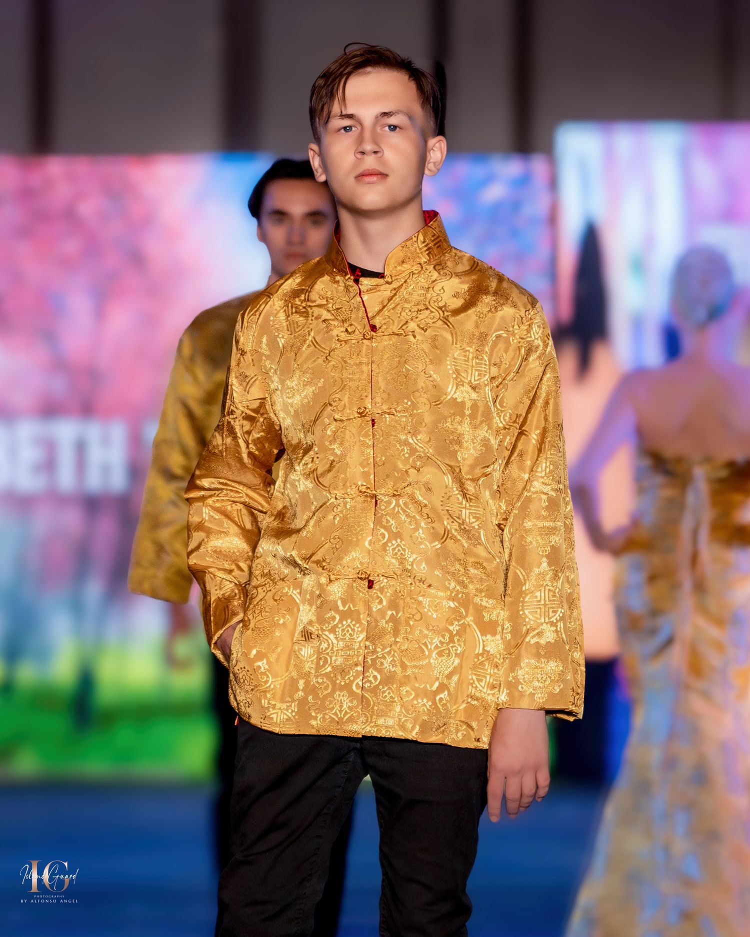 Model presents gold brocade jacket with mandarin collar over black pants.