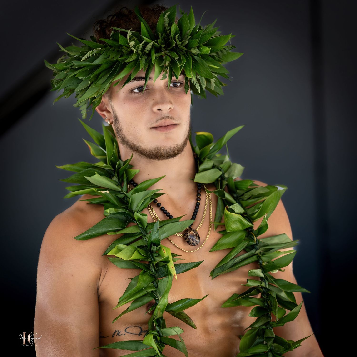 Portrait of person adorned with green leaf lei against dark studio background.