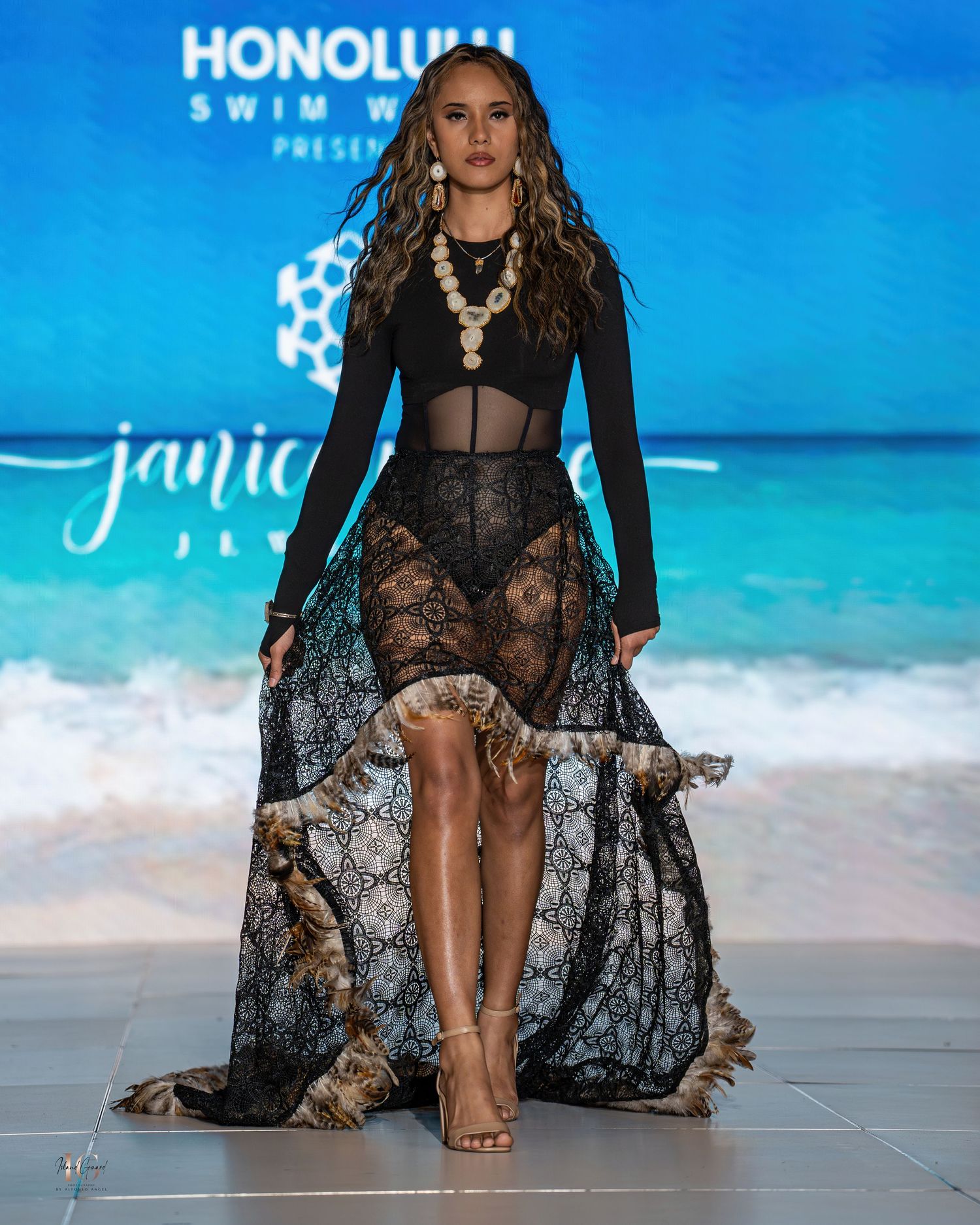 Model in sheer black lace gown walks runway at Honolulu Swim Week.