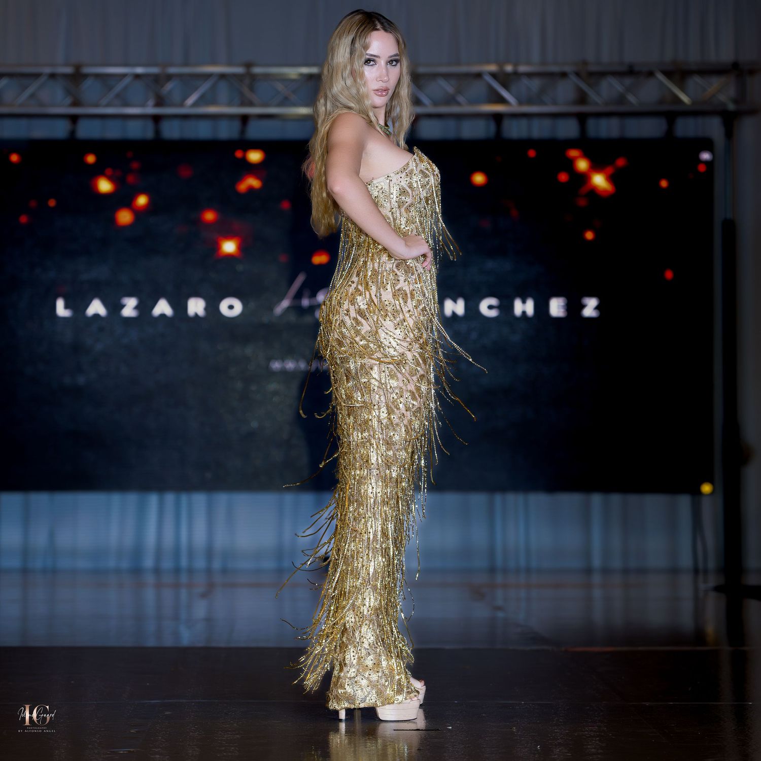 Metallic gold fringed evening gown sparkles under dramatic runway lighting.