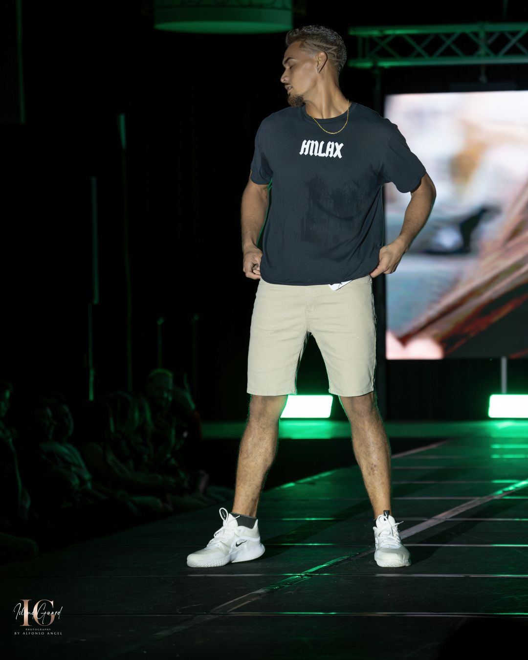 Model in dark shirt and khaki shorts poses on illuminated runway.