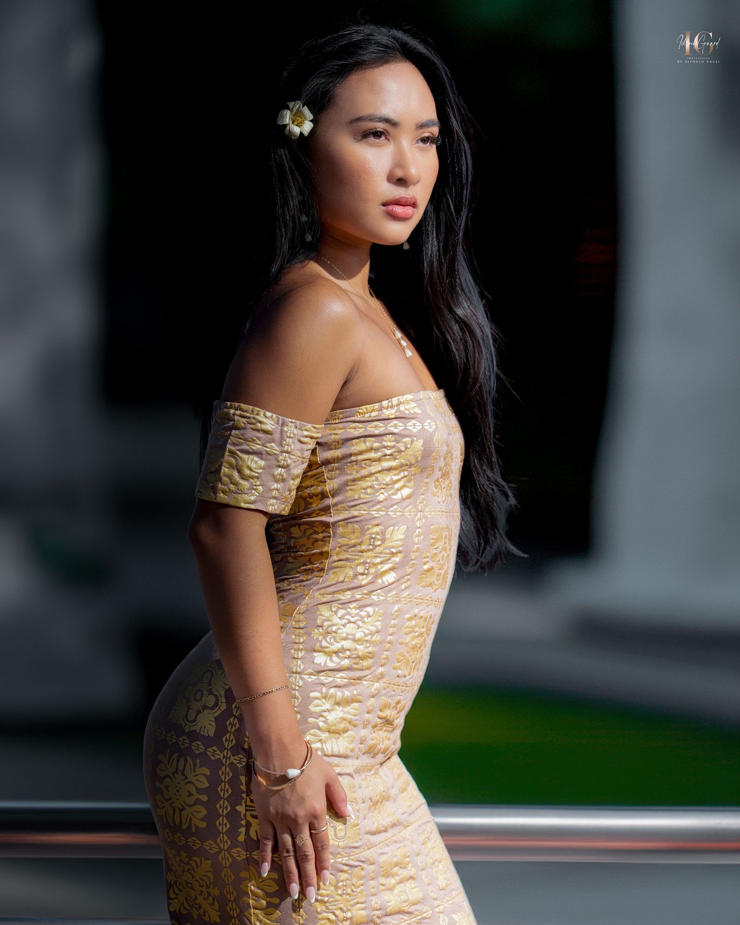 A person in a shimmering gold off-shoulder dress poses elegantly against a dark background.