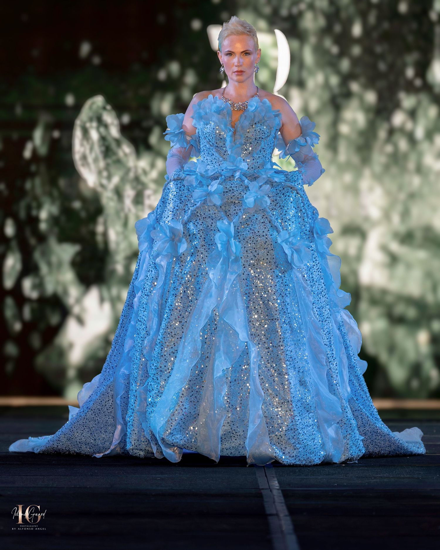 Ethereal blue glittering ball gown with sheer details and dramatic silhouette against textured backdrop.