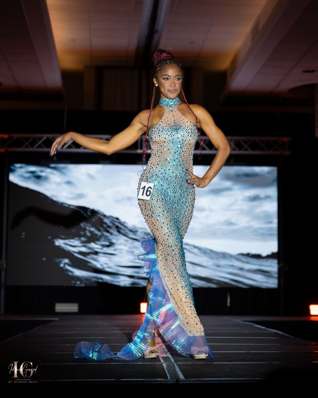 A contestant in a sparkly blue-silver gown strikes a pose on a runway during a fashion show competition.