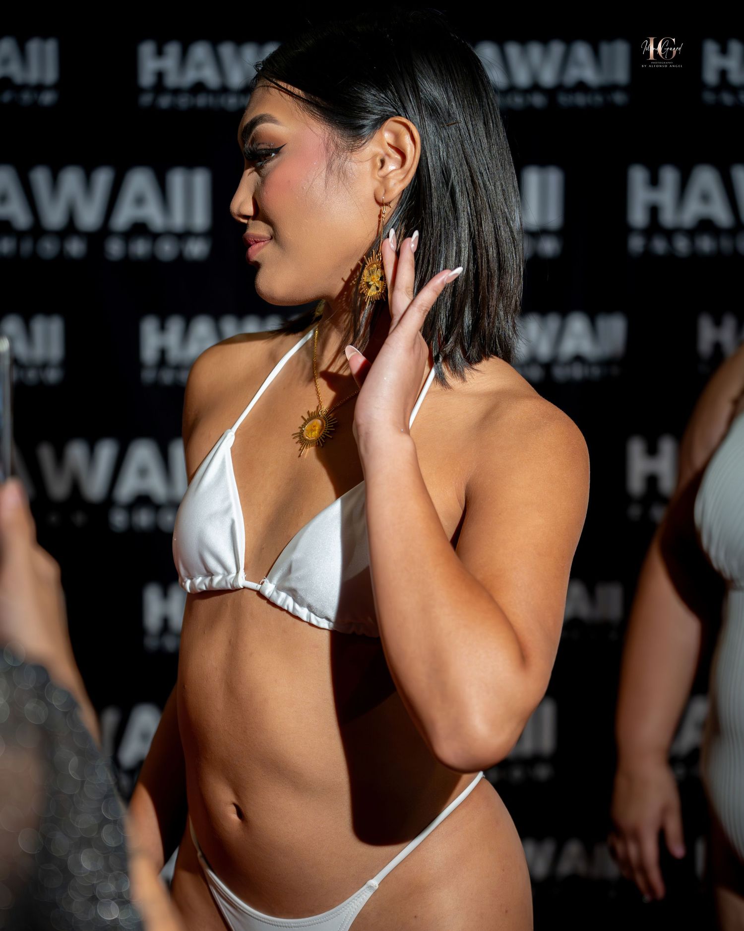 A person in a white bikini top poses against a dark backdrop at what appears to be a public event.