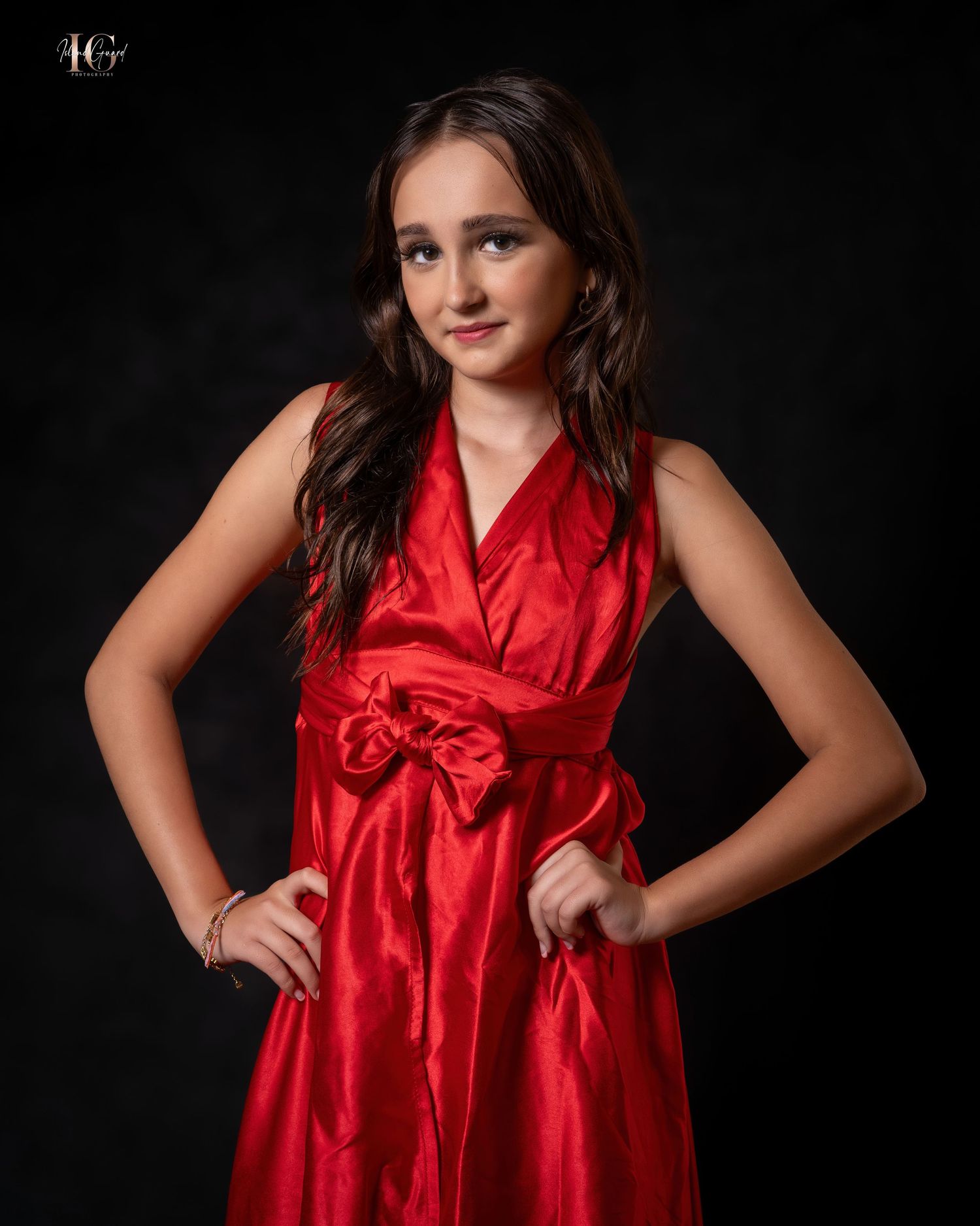 Studio portrait of someone in a vibrant red satin dress with bow detail against a dark background.