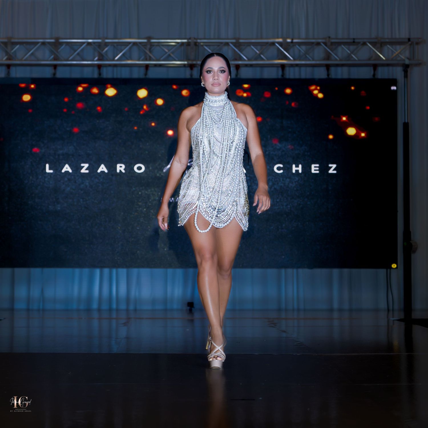 Models showcase elegant white evening wear on dark runway with sparkling lights.