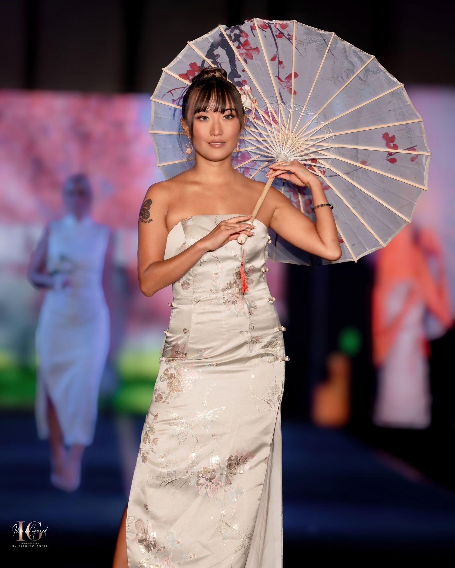 Model showcases traditional Asian-inspired white dress with parasol on fashion runway.