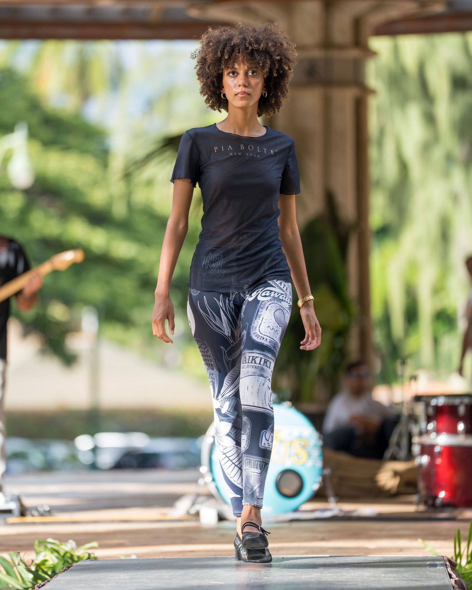 Person in a black shirt and patterned leggings performs a dynamic dance move on an outdoor patio.