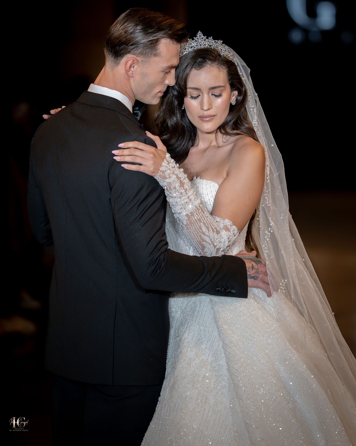 A couple shares an intimate moment during their wedding celebration, with the bride wearing a sparkling white gown and veil.