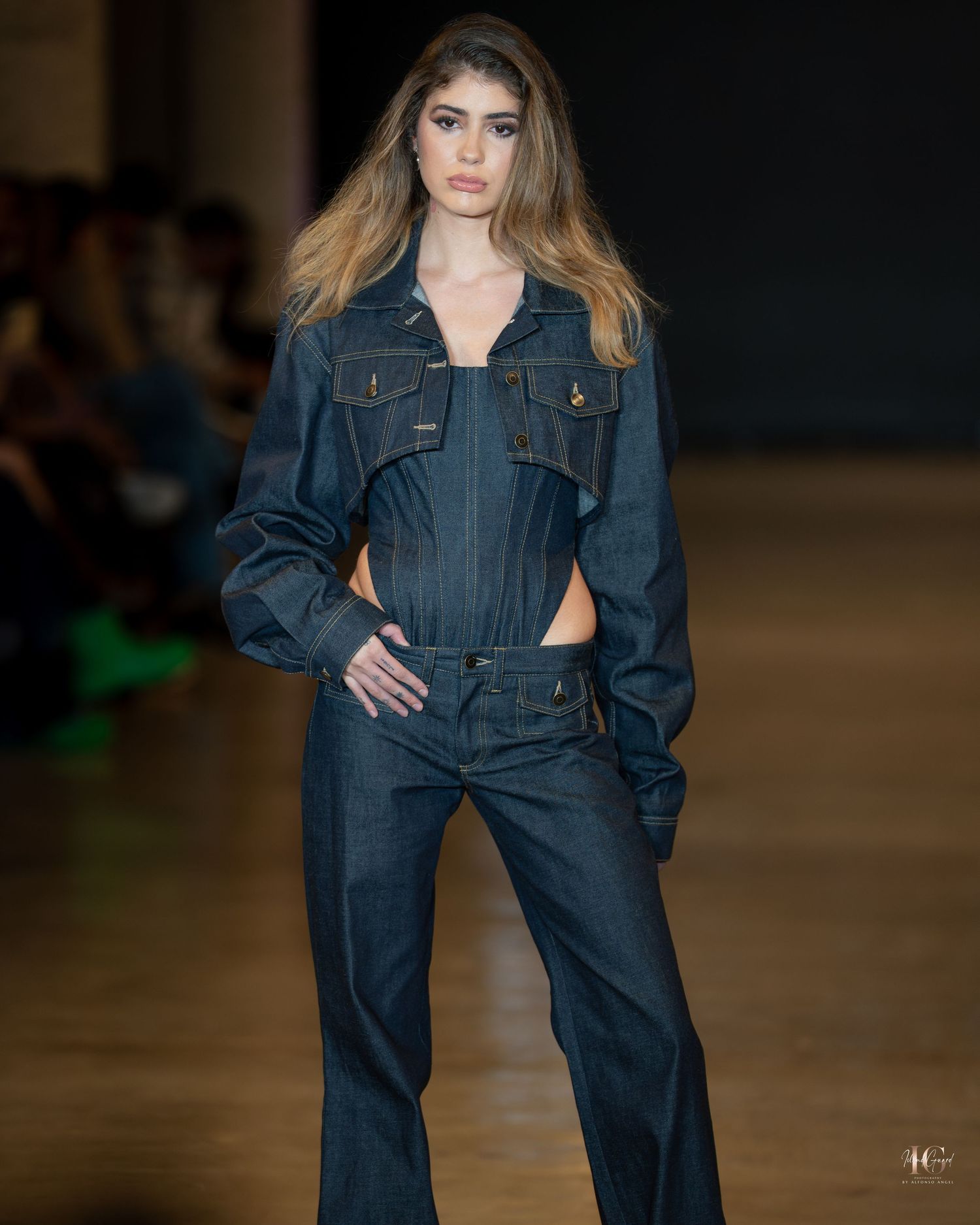 Model showcases dark denim coordinated outfit with cropped jacket and wide-leg pants on wooden runway.