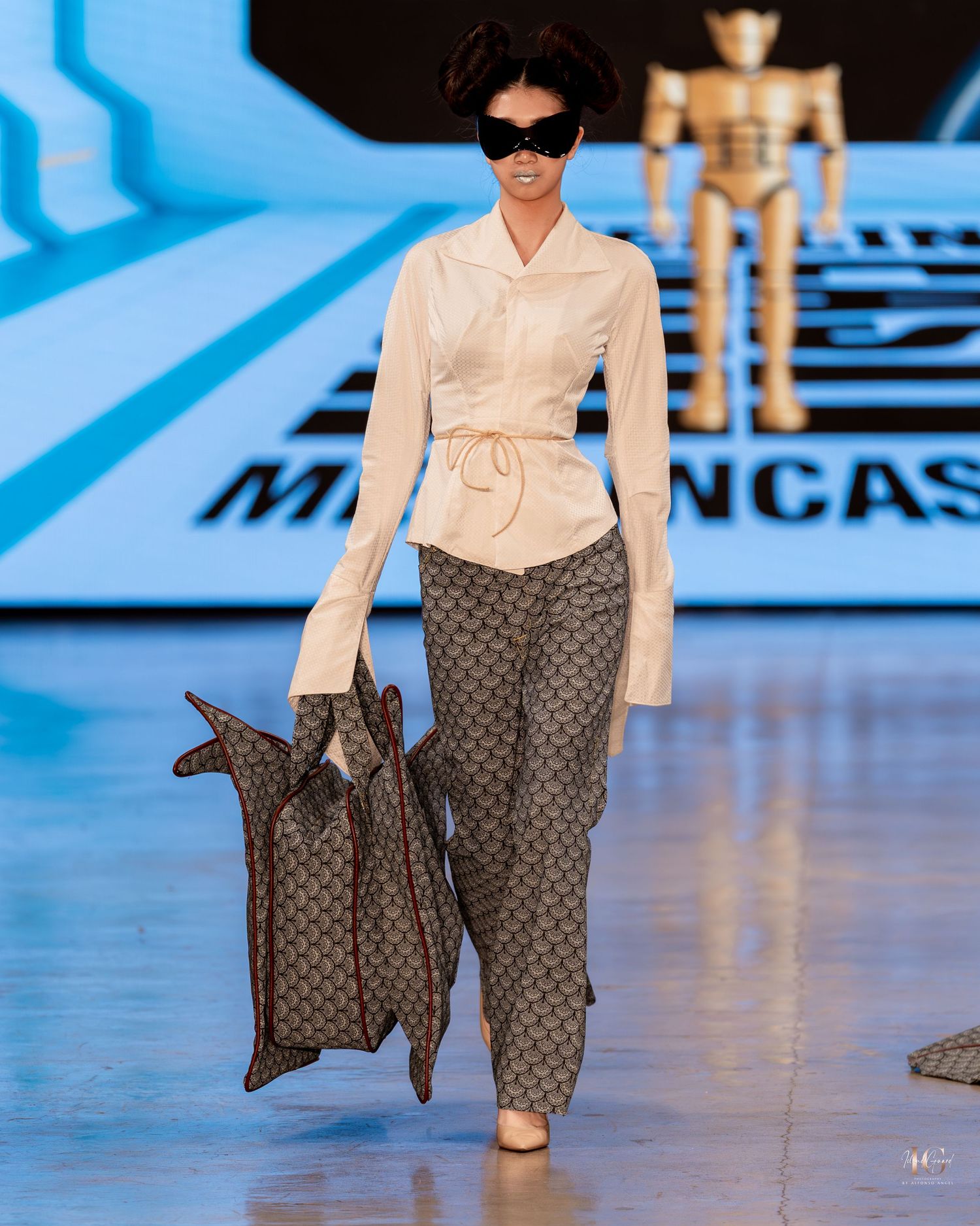 Fashion model walks runway wearing cream silk blouse and Louis Vuitton monogram pants with matching handbag.