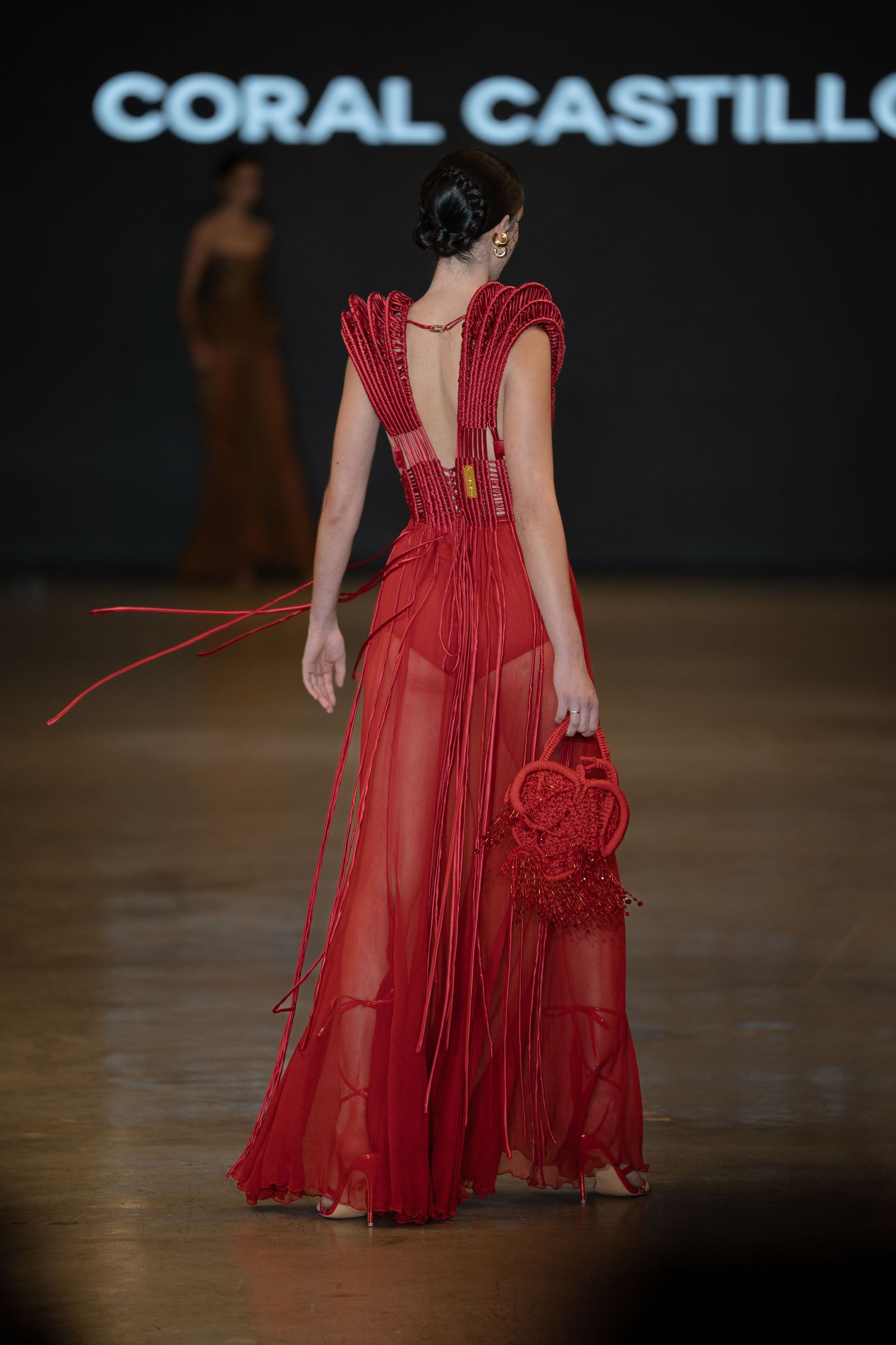 A model walks the runway in a flowing red sheer gown with dramatic ruffled details from the Coral Castillo collection.