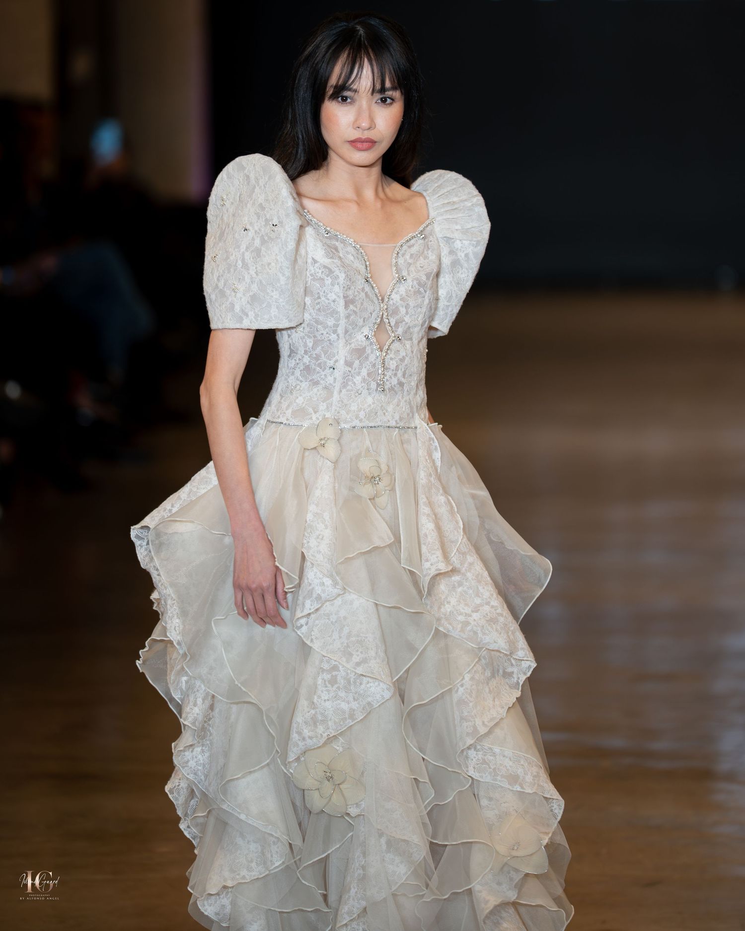 Elegant white wedding gown with puff sleeves, lace bodice and tiered ruffled skirt shown on runway.