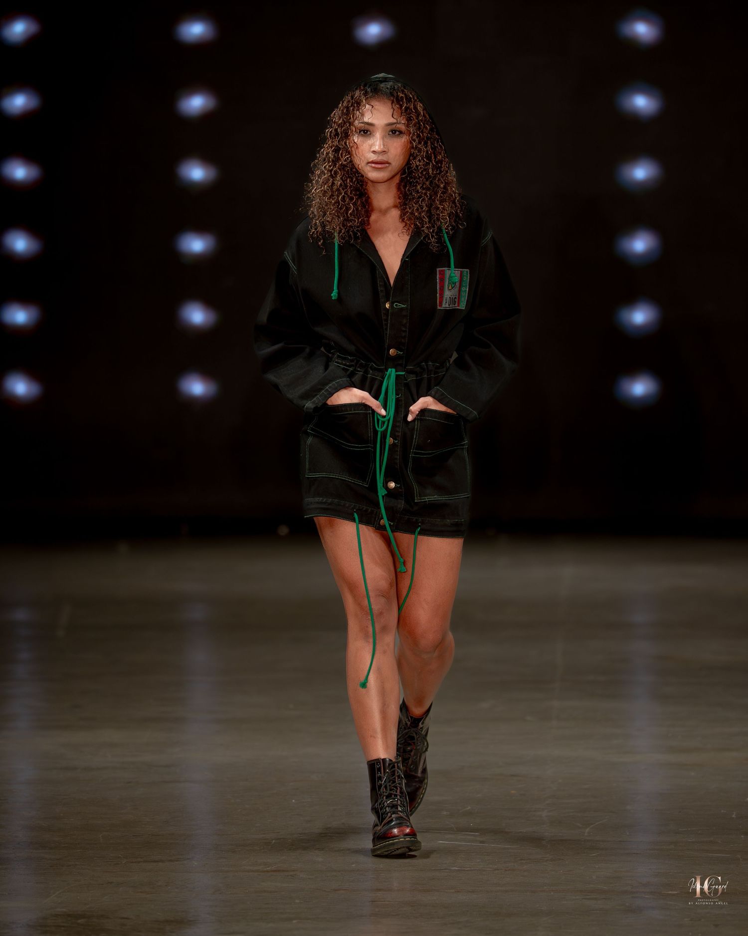 Model walks runway in dark green velvet mini dress with combat boots during fashion show.