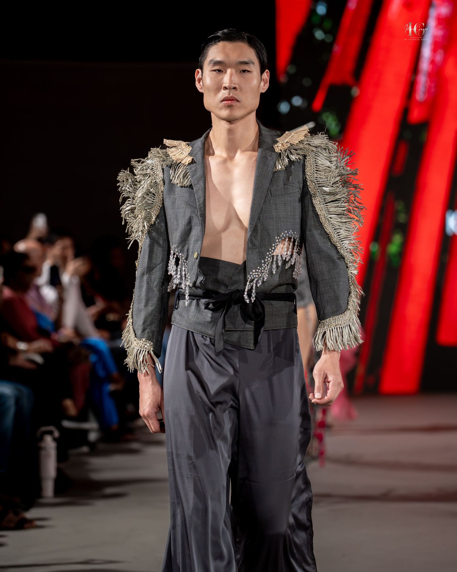 Models walk runway in avant-garde black and grey deconstructed fashion designs against dramatic red backdrop at fashion show.