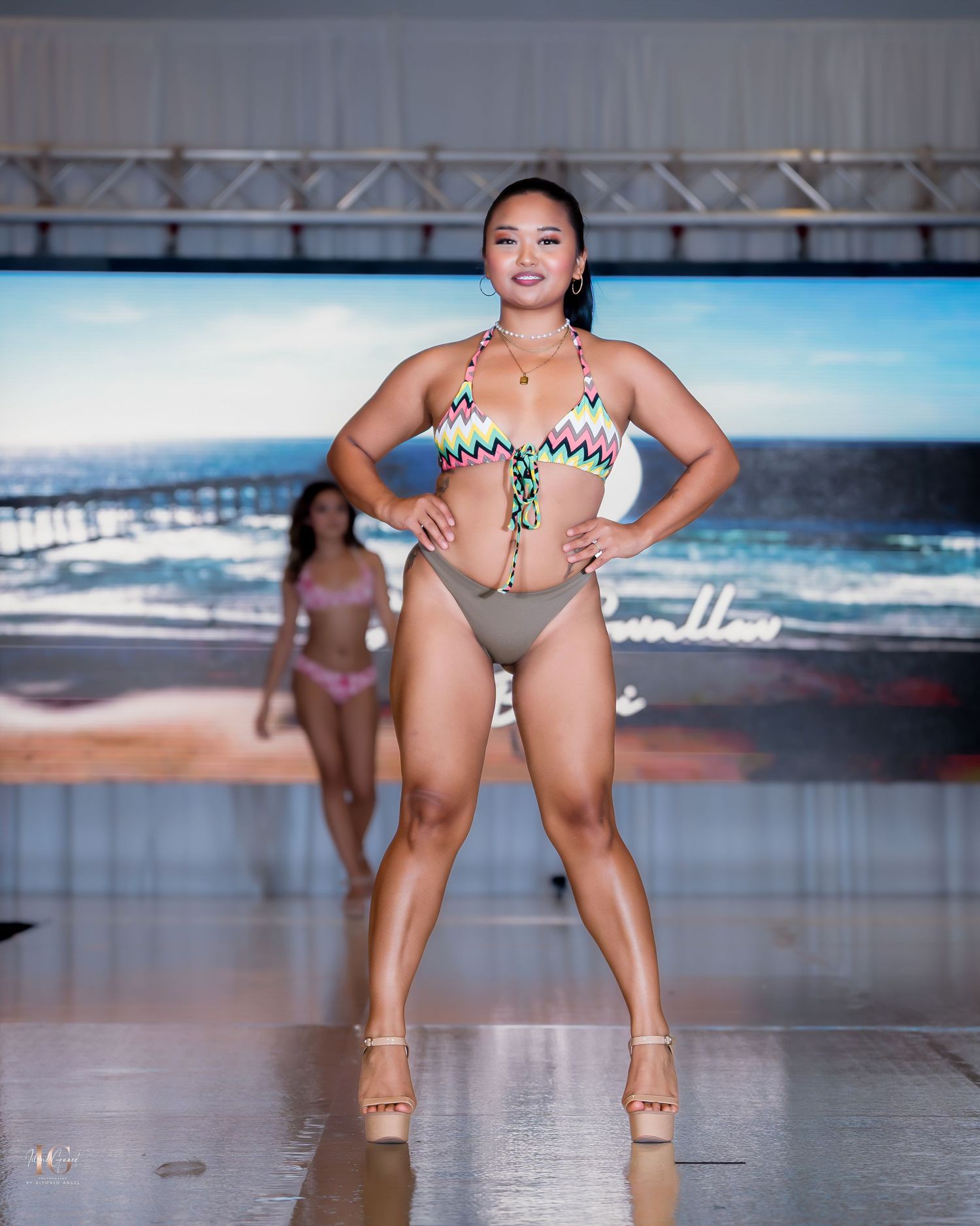 Model presents geometric print swimwear on beach-themed runway.