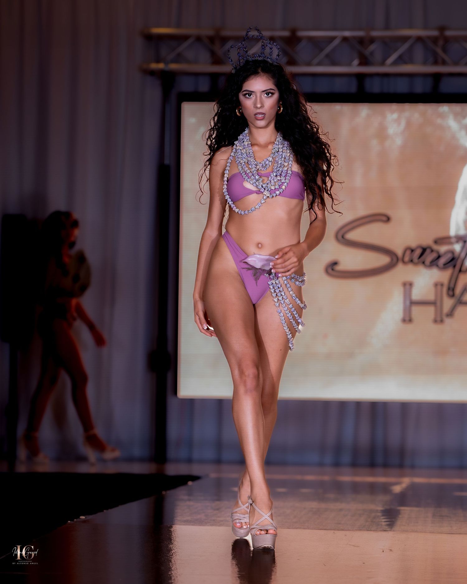 Fashion models display purple and silver swimwear designs during an evening runway show.