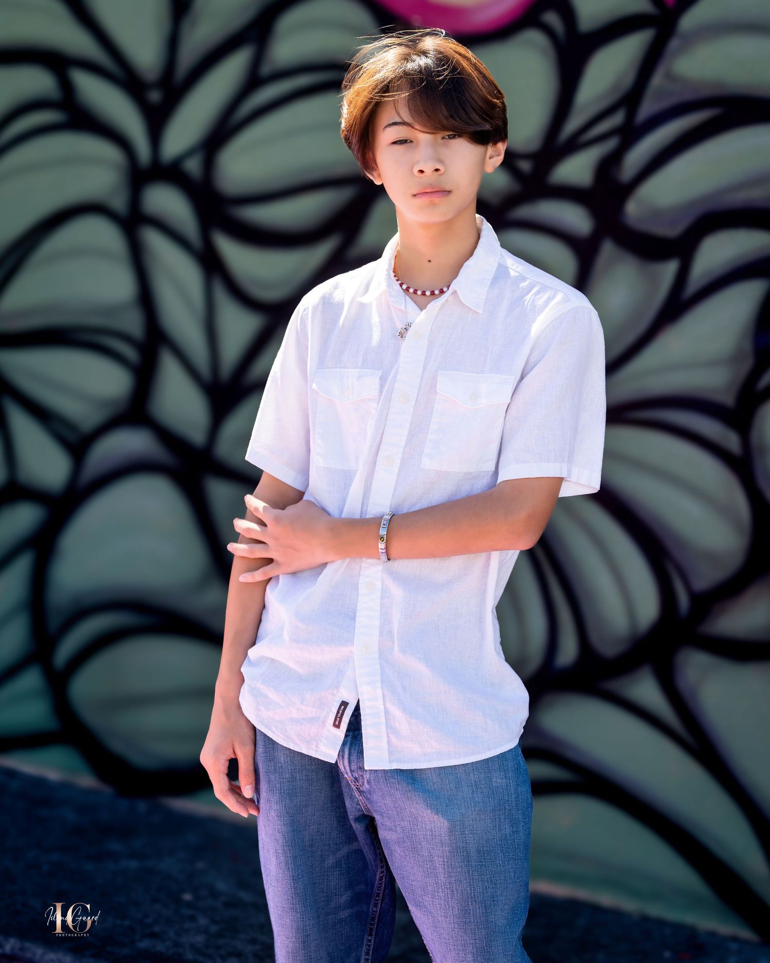 Young person in white button-down shirt poses against decorative wall with leaf patterns.