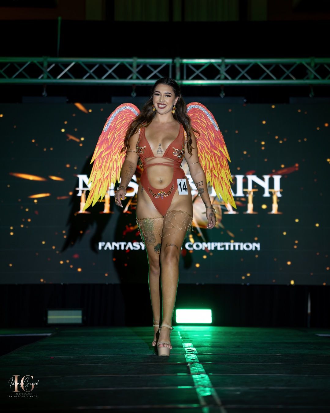 Model walks runway in glowing fantasy-inspired costume with shimmering wings and LED effects on dark stage.